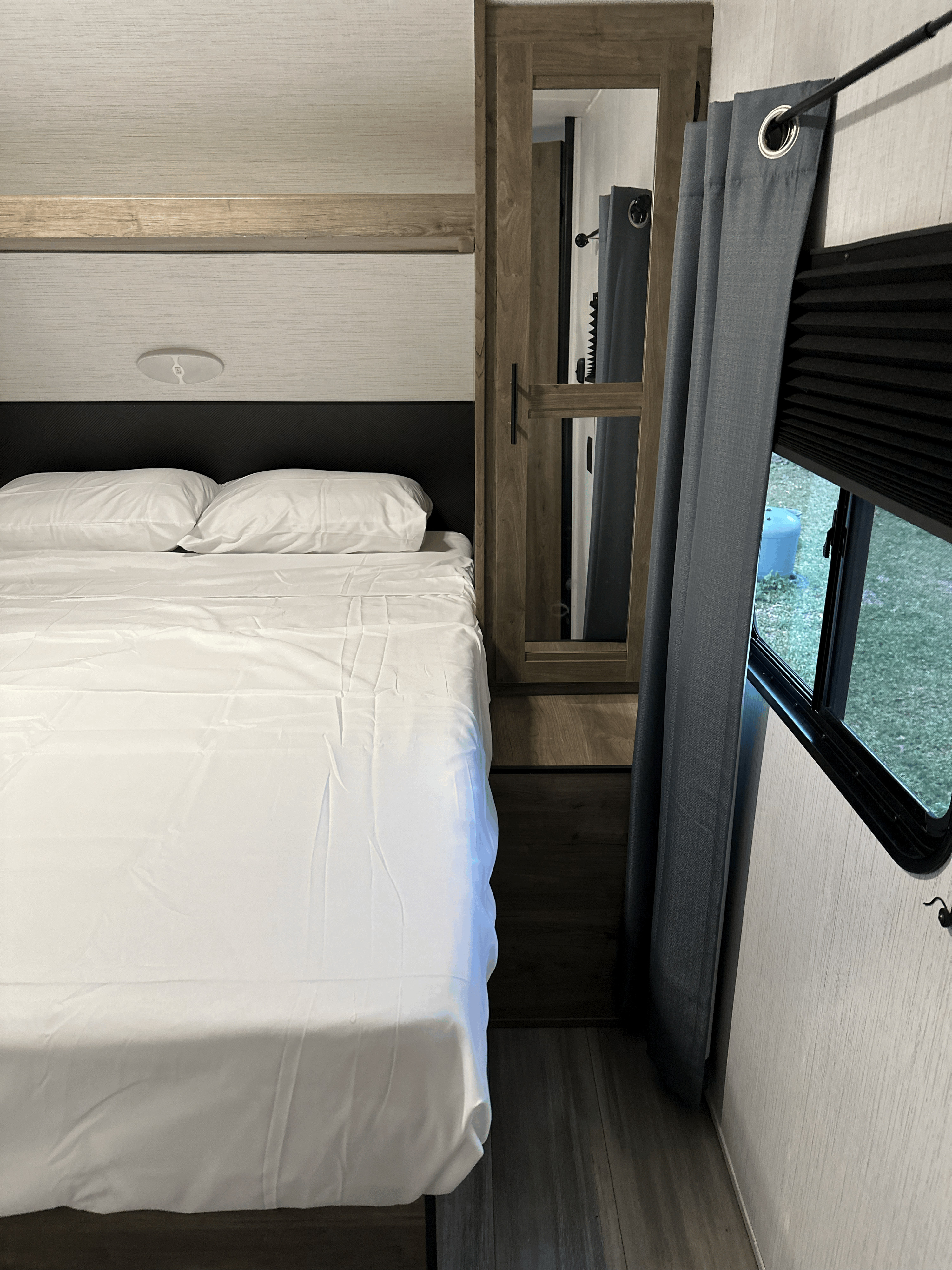 RV rental bedroom: a neat bed with white linens, mirrored cabinet, and window for a compact, comfortable stay.. Heartland RVs Pioneer 2023