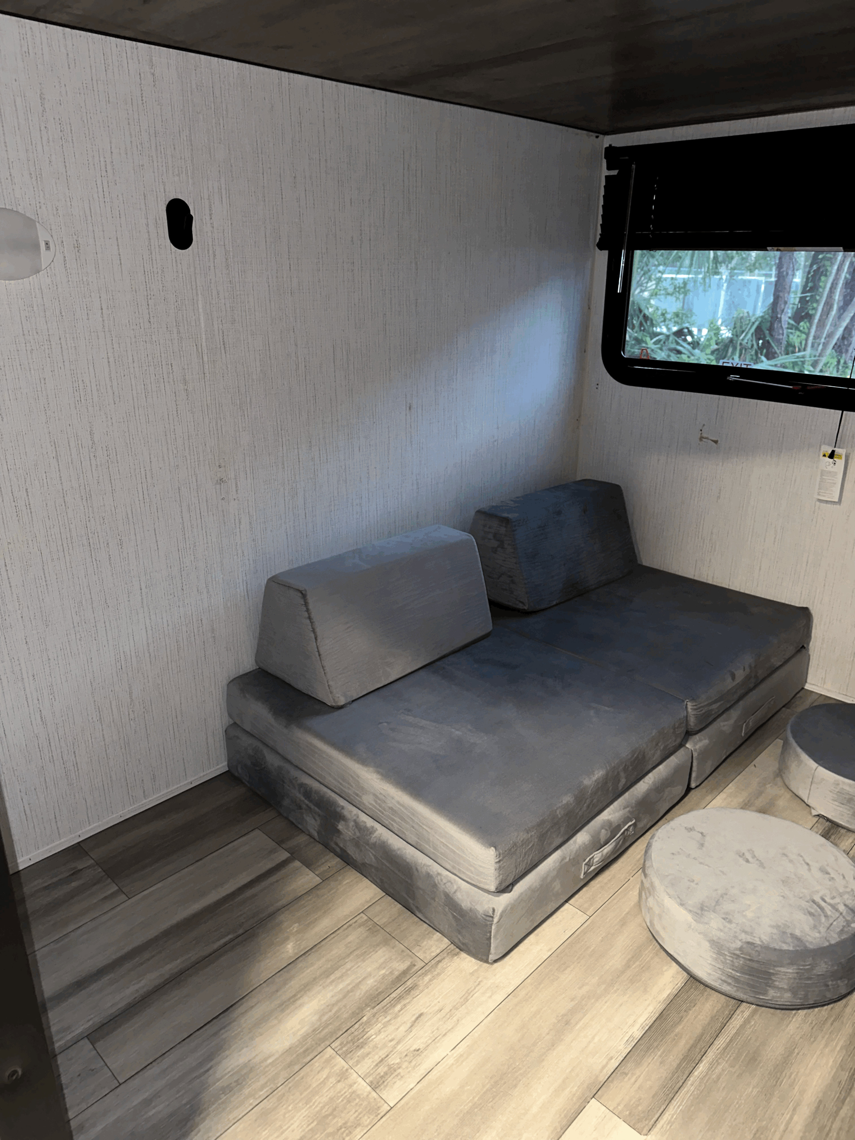 RV rental interior features grey modular seating, two round ottomans, wood-look flooring, and a window view.. Heartland RVs Pioneer 2023