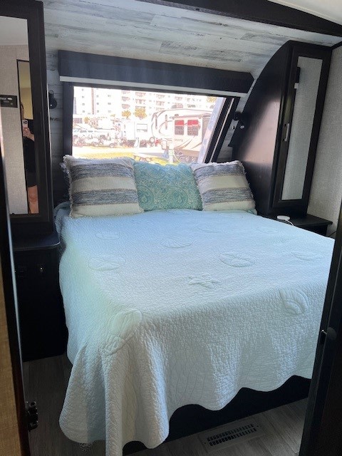 Experience comfort in this RV rental bedroom. Features a white quilted bed, throw pillows, and a large window with an outdoor view.. Jayco White Hawk 2022
