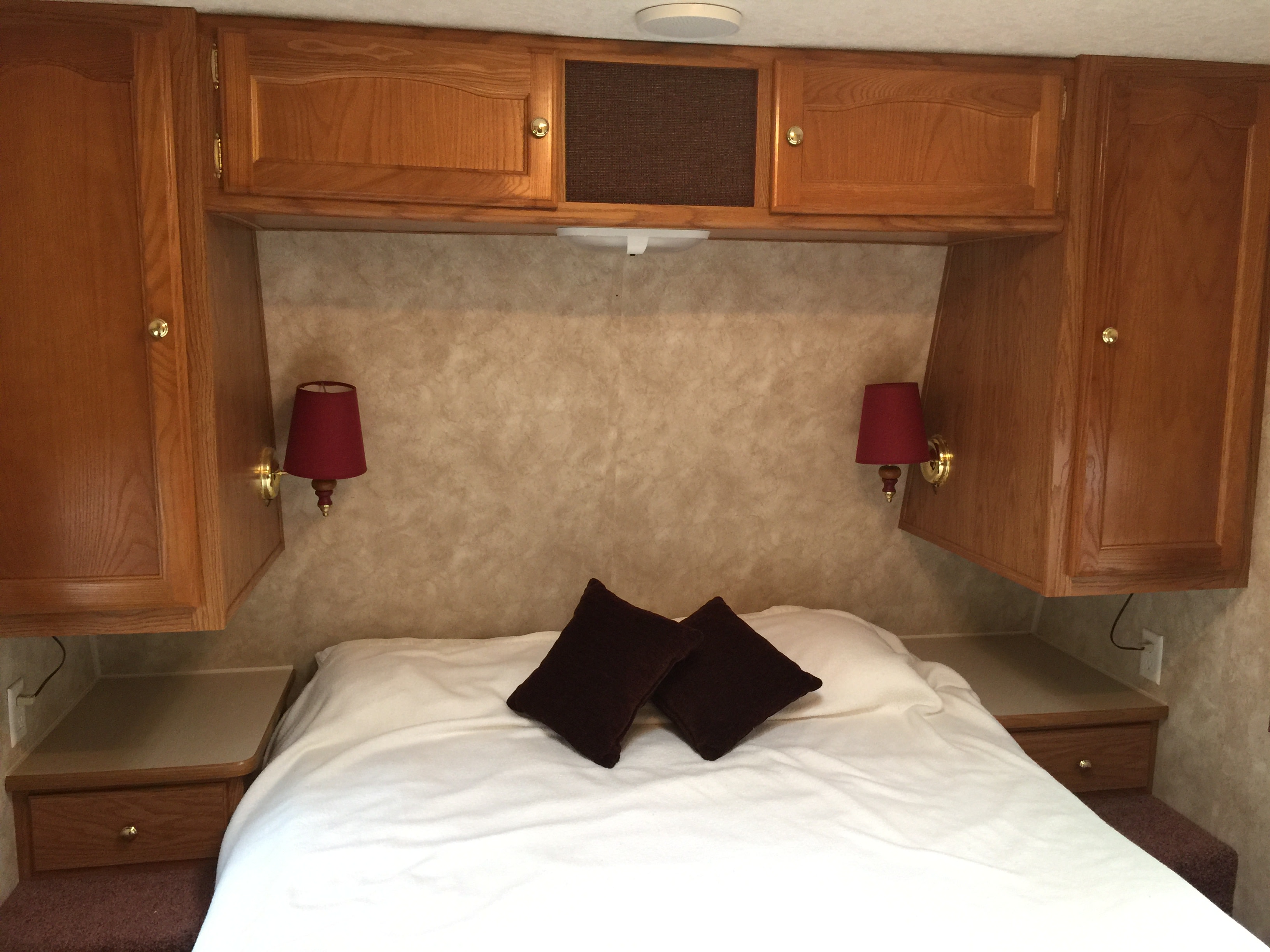 RV rental: A compact bedroom featuring a bed, built-in wooden cabinets overhead, wall lamps, and convenient nightstands.. Keystone RV Springdale 2005