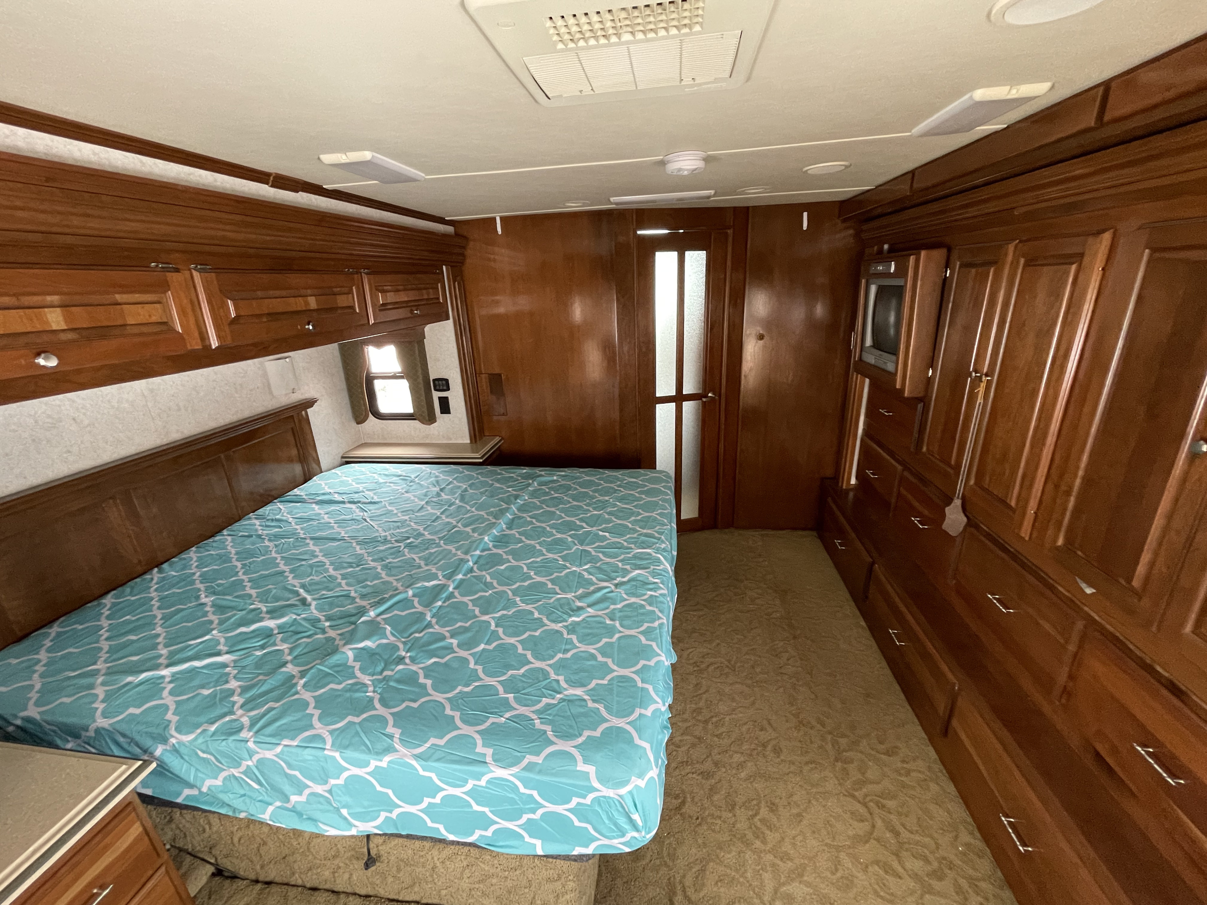 Comfortable RV rental bedroom featuring a bed with a blue patterned comforter, rich wooden cabinetry, and AC.. Monaco Camelot 2007
