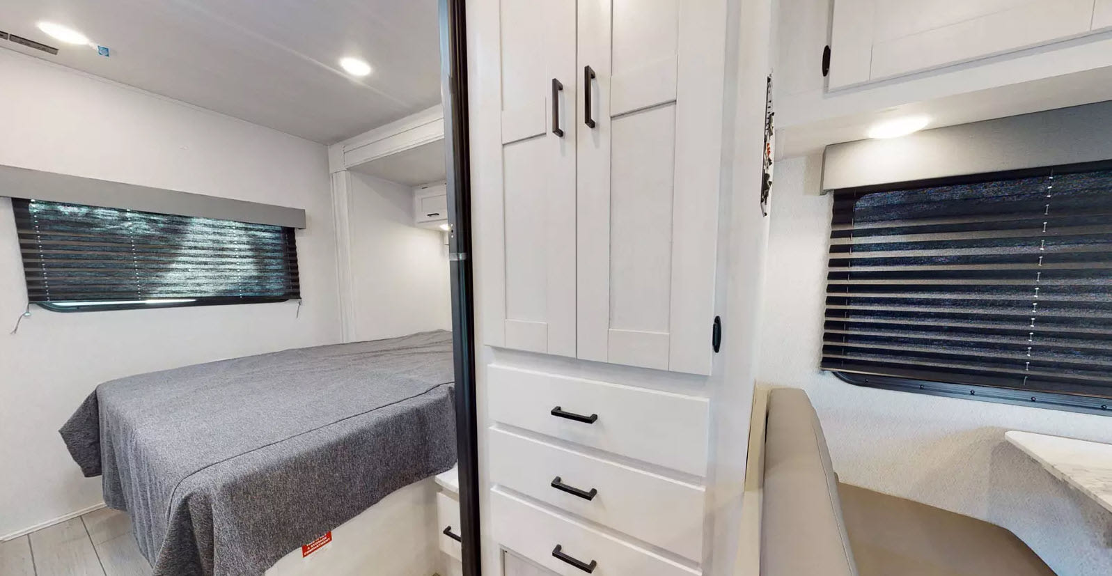 Cozy RV rental interior with bed, storage cabinets, and bright windows, offering comfortable compact living.. East to West 220SC 2025