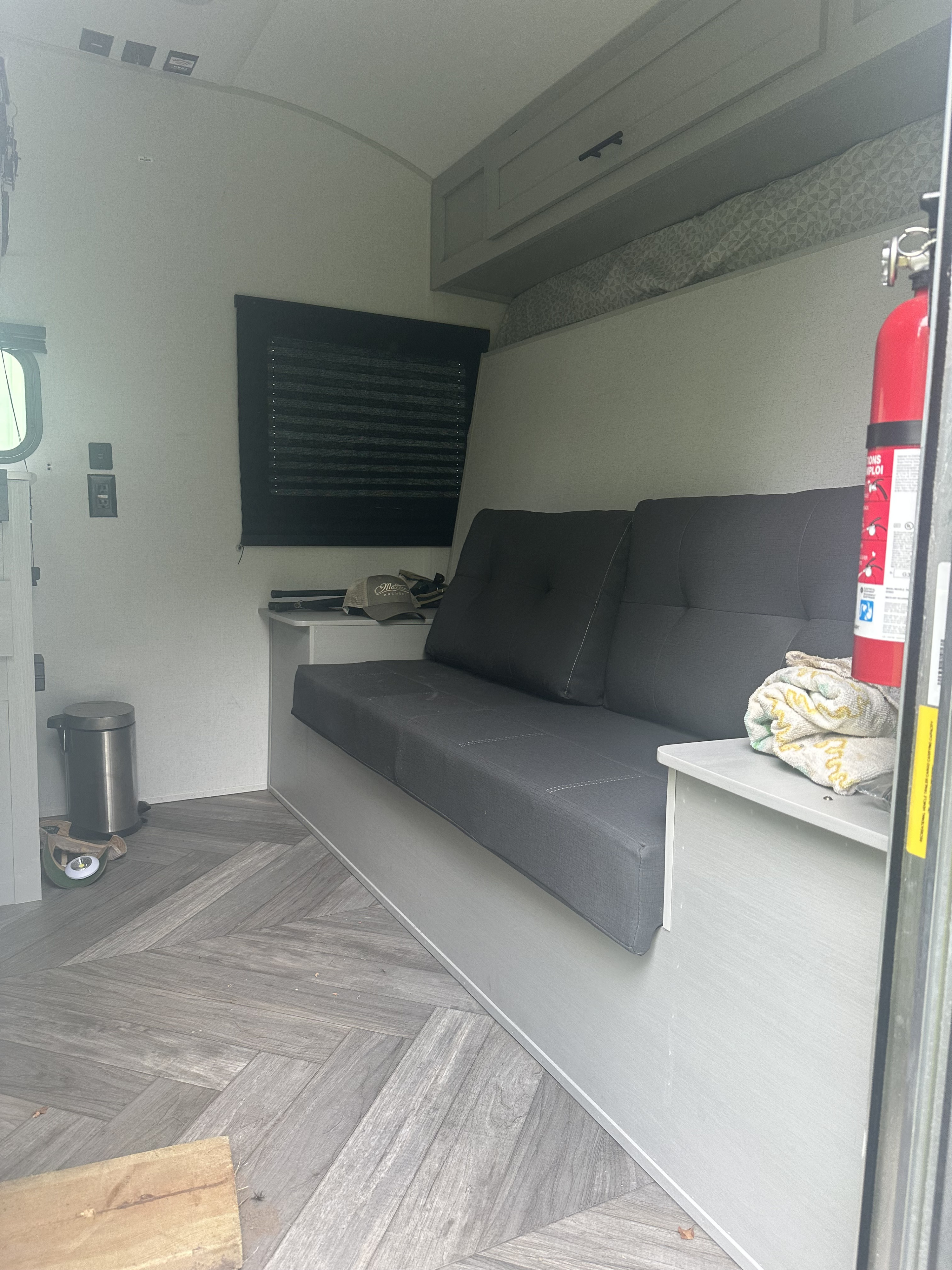 Inside an RV rental: a modern gray futon, herringbone-patterned floor, overhead cabinets, and a fire extinguisher.. Forest River Wildwood FSX Platinum 2021