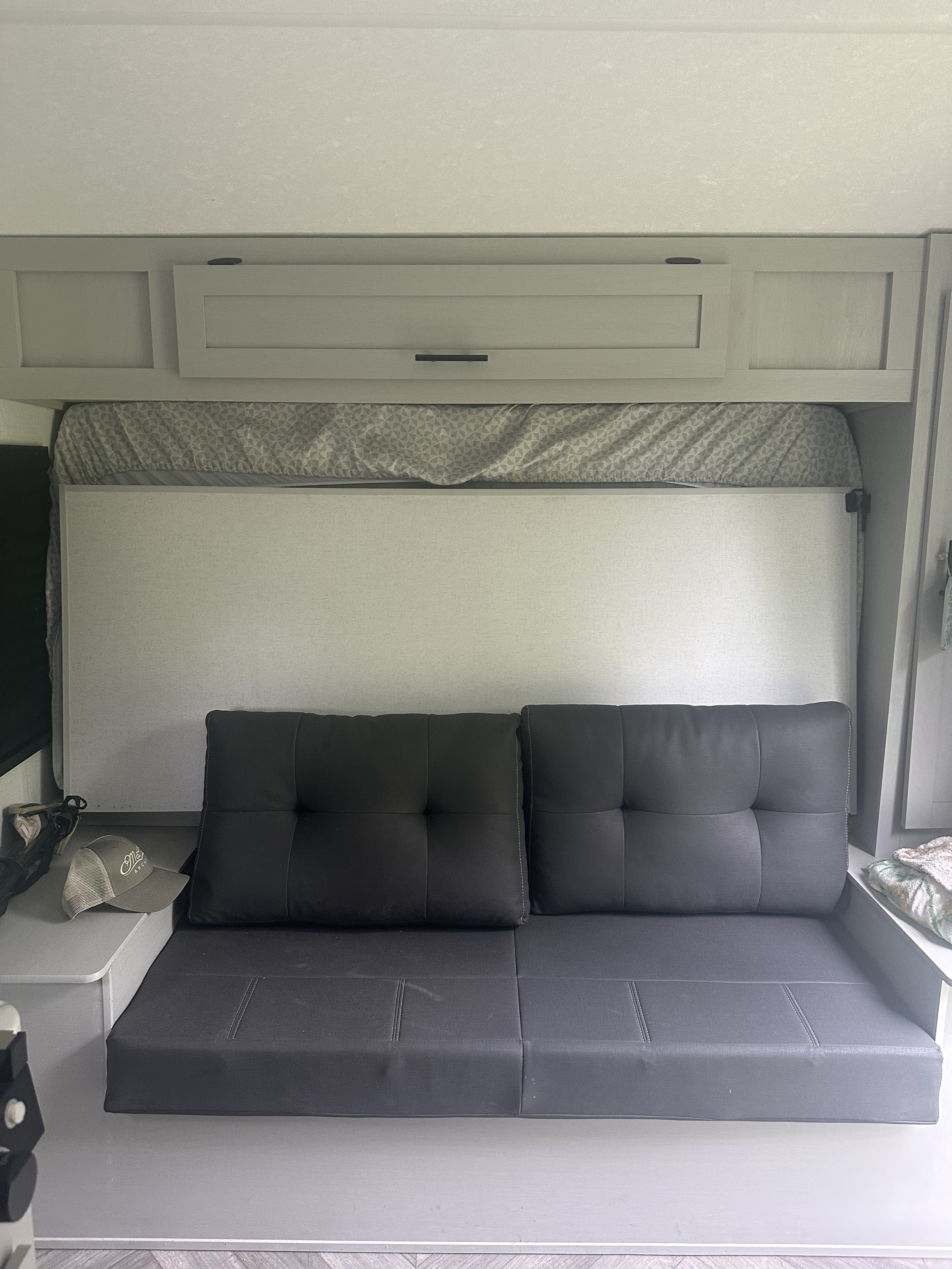 RV rental's versatile living area: a comfortable gray sofa below a neatly tucked-away mattress and storage cabinets.. Forest River Wildwood FSX Platinum 2021