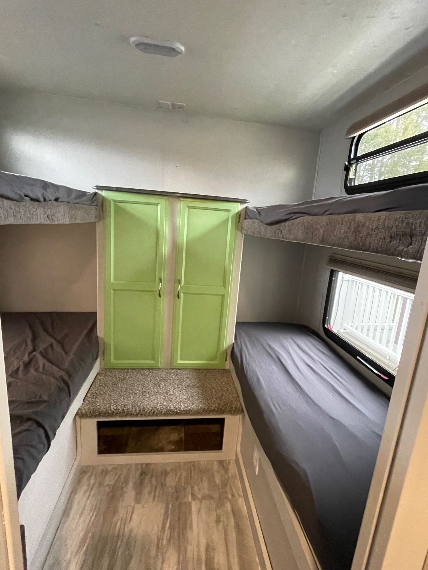 RV rental interior featuring a bunk room with four gray-sheeted beds, a central green cabinet, and windows.. Coachmen Freedom Express 29SE 2017
