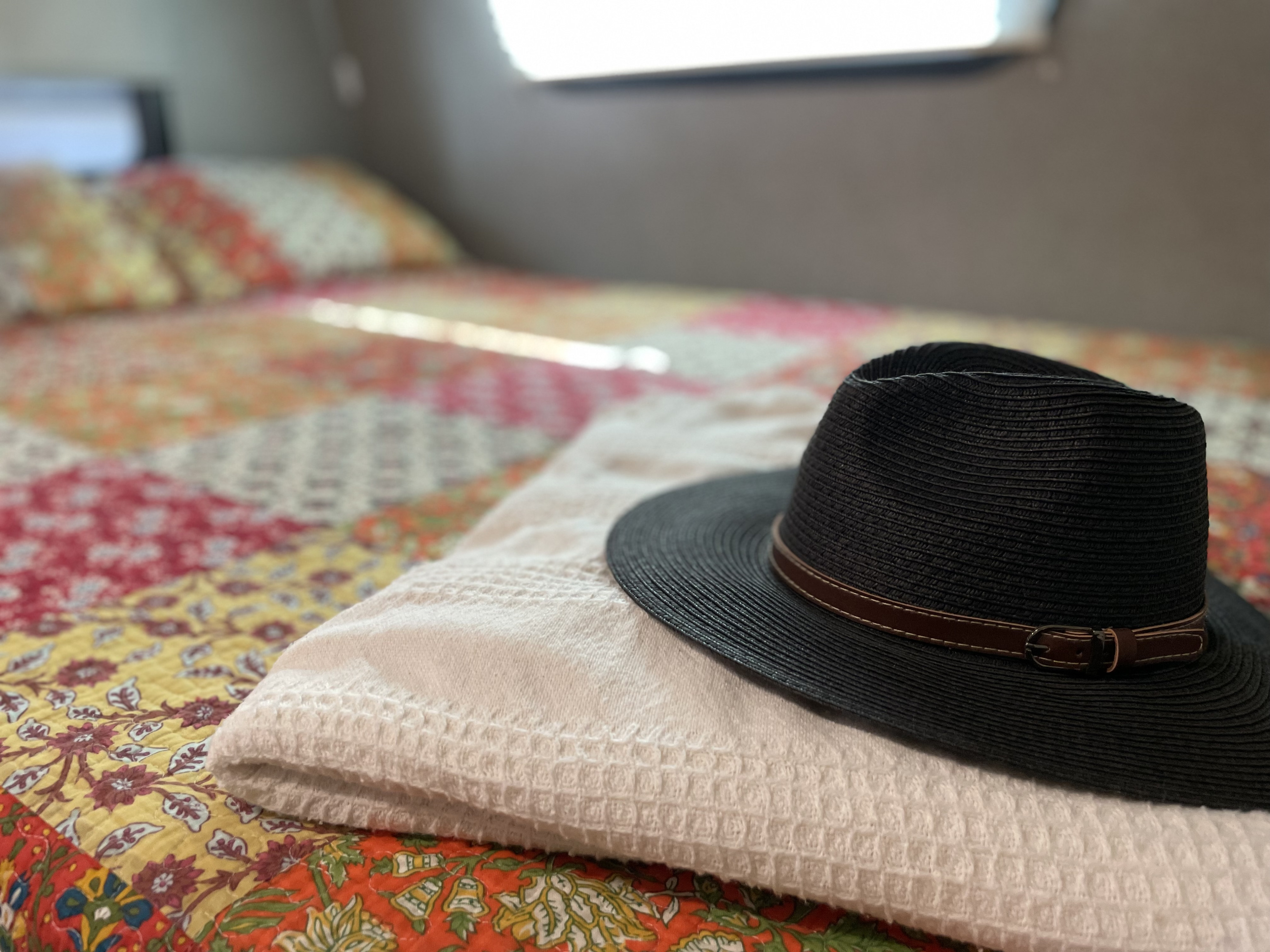 RV rental bedroom: A black woven hat on a white towel, atop a colorful quilted bedspread, offers cozy comfort.. Forest River Flagstaff E-Pro 2021