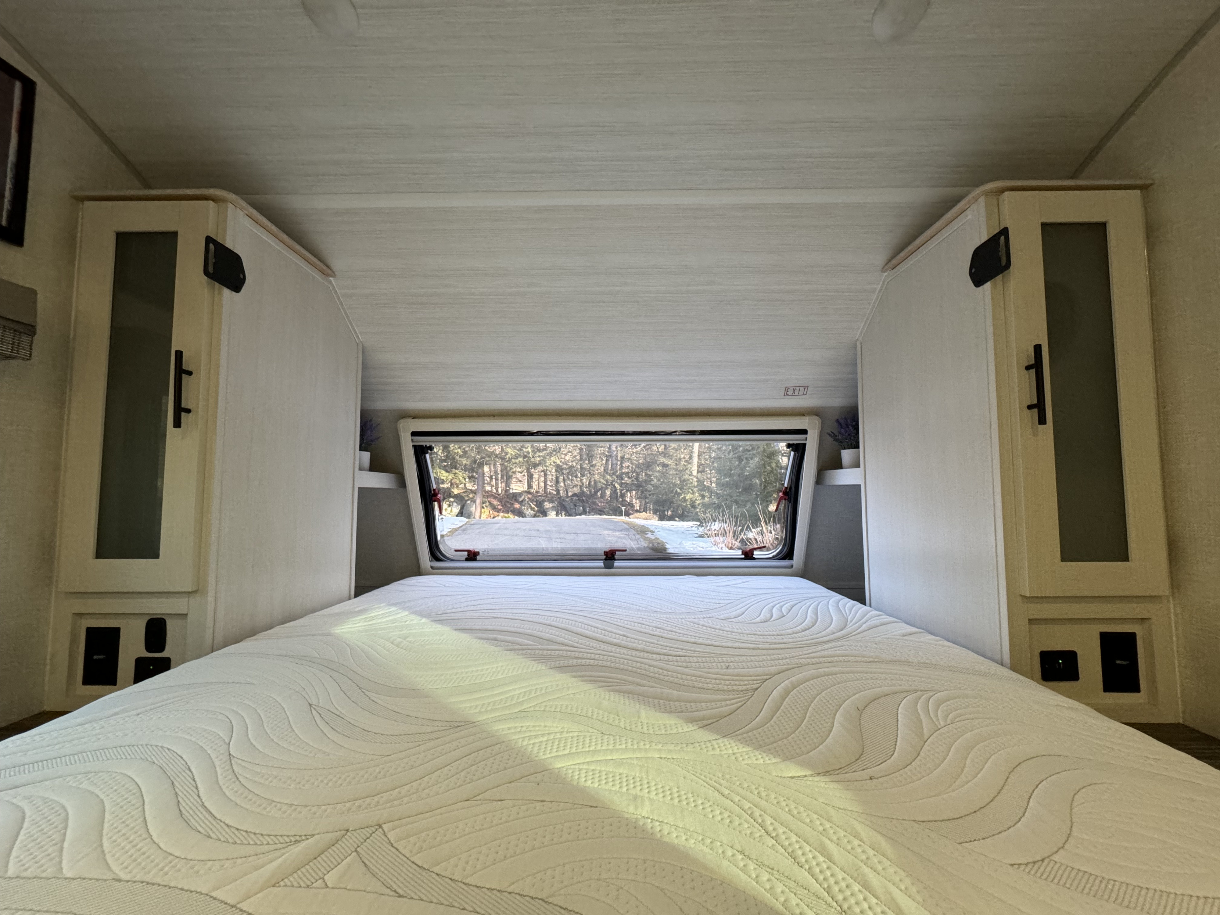 Inside a bright **RV rental** bedroom with a large bed, modern light-wood cabinets, and a scenic window view of a snowy forest.. R-Pod R-Pod Trailer 2022