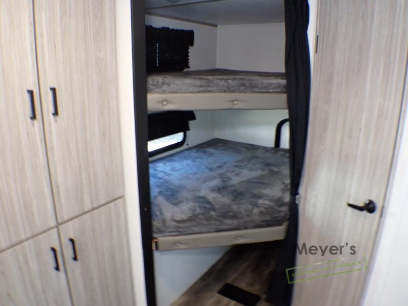Inside an RV rental: Two cozy bunk beds with grey bedding and light wood storage cabinets.. Keystone RV Passport SL 2022