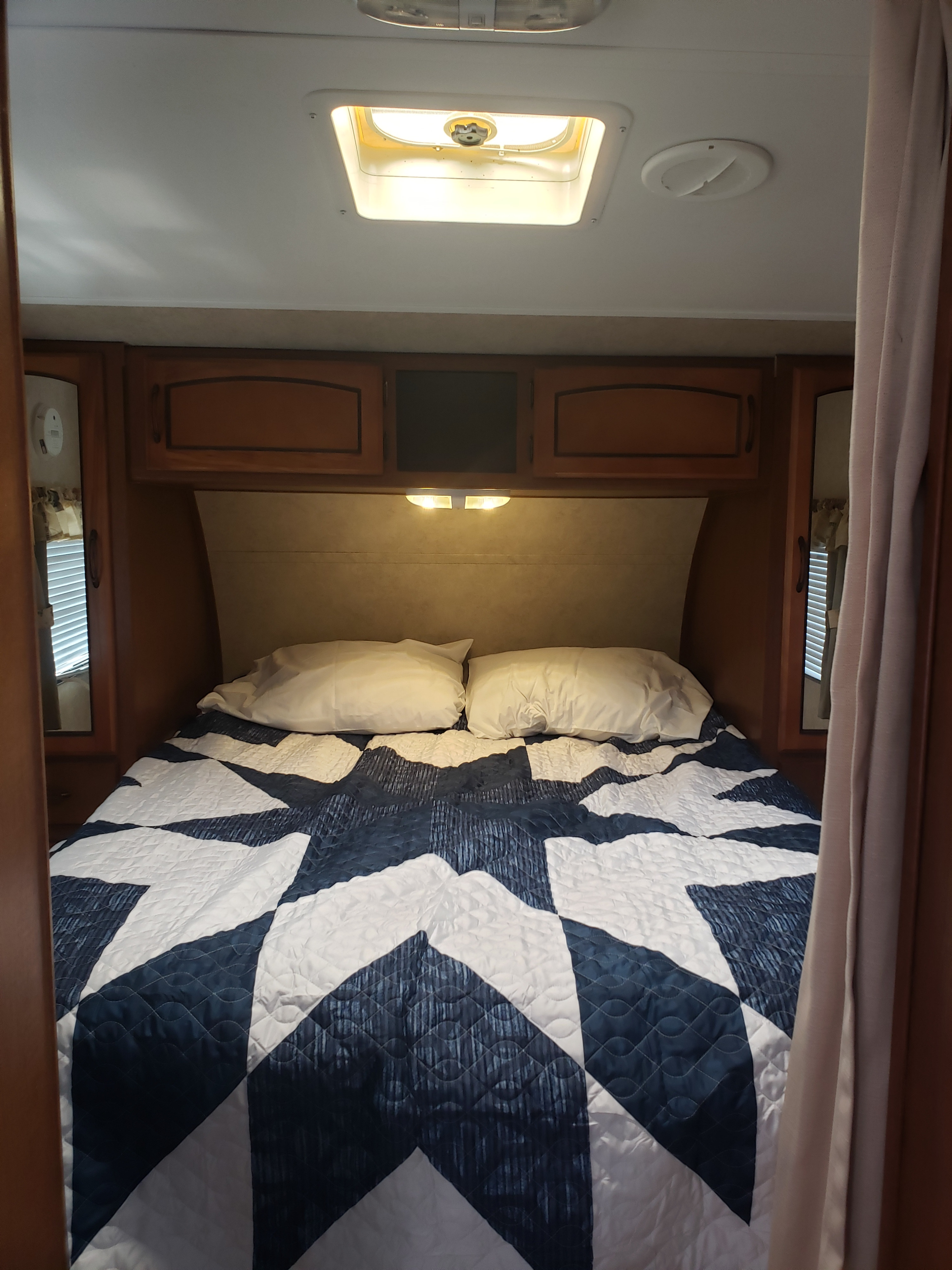Experience comfort in this RV rental bedroom: blue/white quilted bed, wood cabinetry, and ceiling vents for a cozy trip.. Keystone RV Springdale 2013