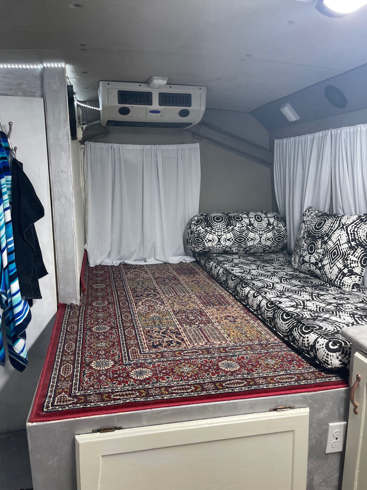 Explore this cozy RV rental interior: a black & white patterned bed, vibrant rug, and AC unit create a comfy space.. Ford E450 2011
