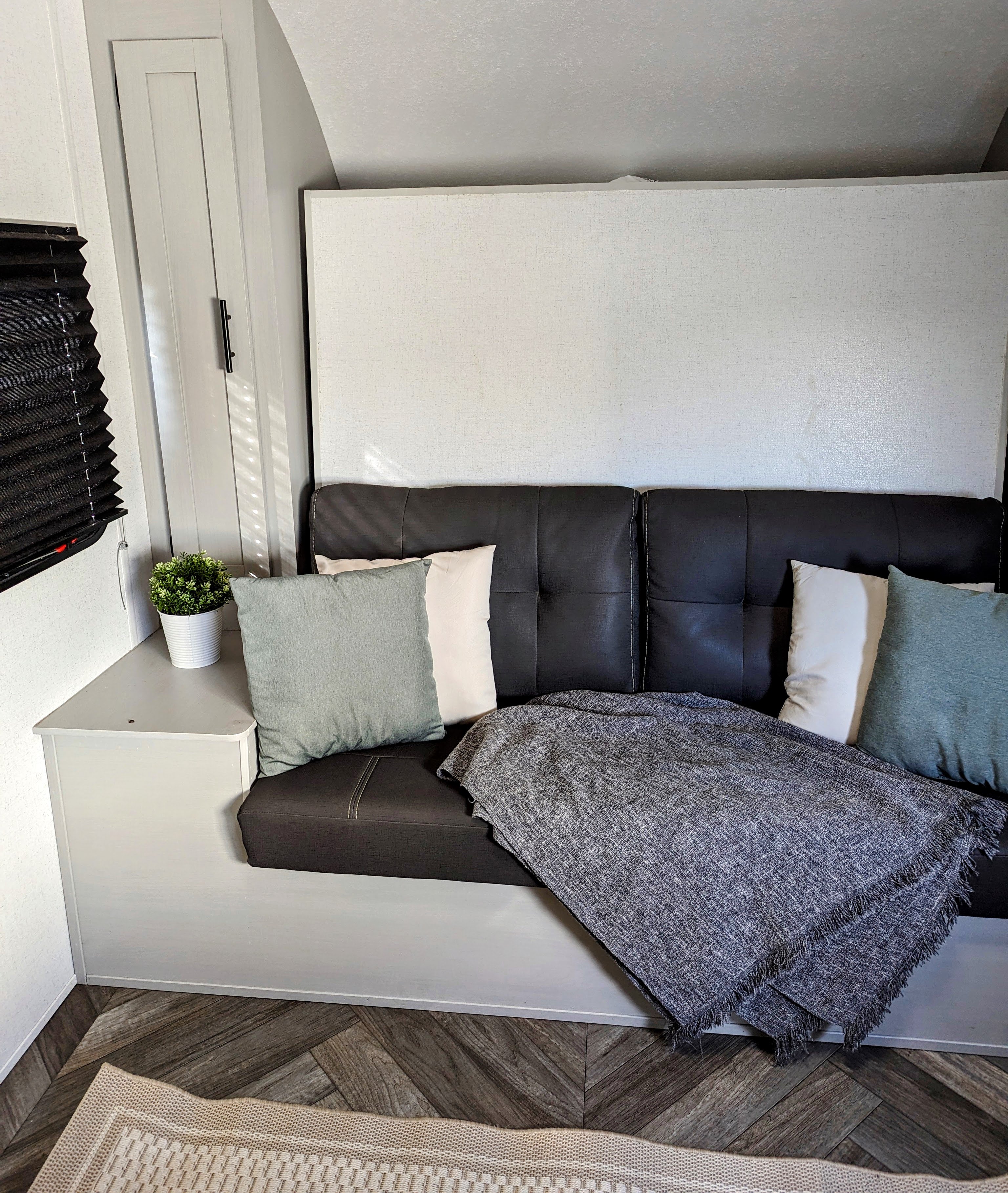 RV rental's inviting interior: sleek dark sofa with light pillows, a soft throw, and a small plant for homey comfort.. Forest River Wildwood FSX 2021