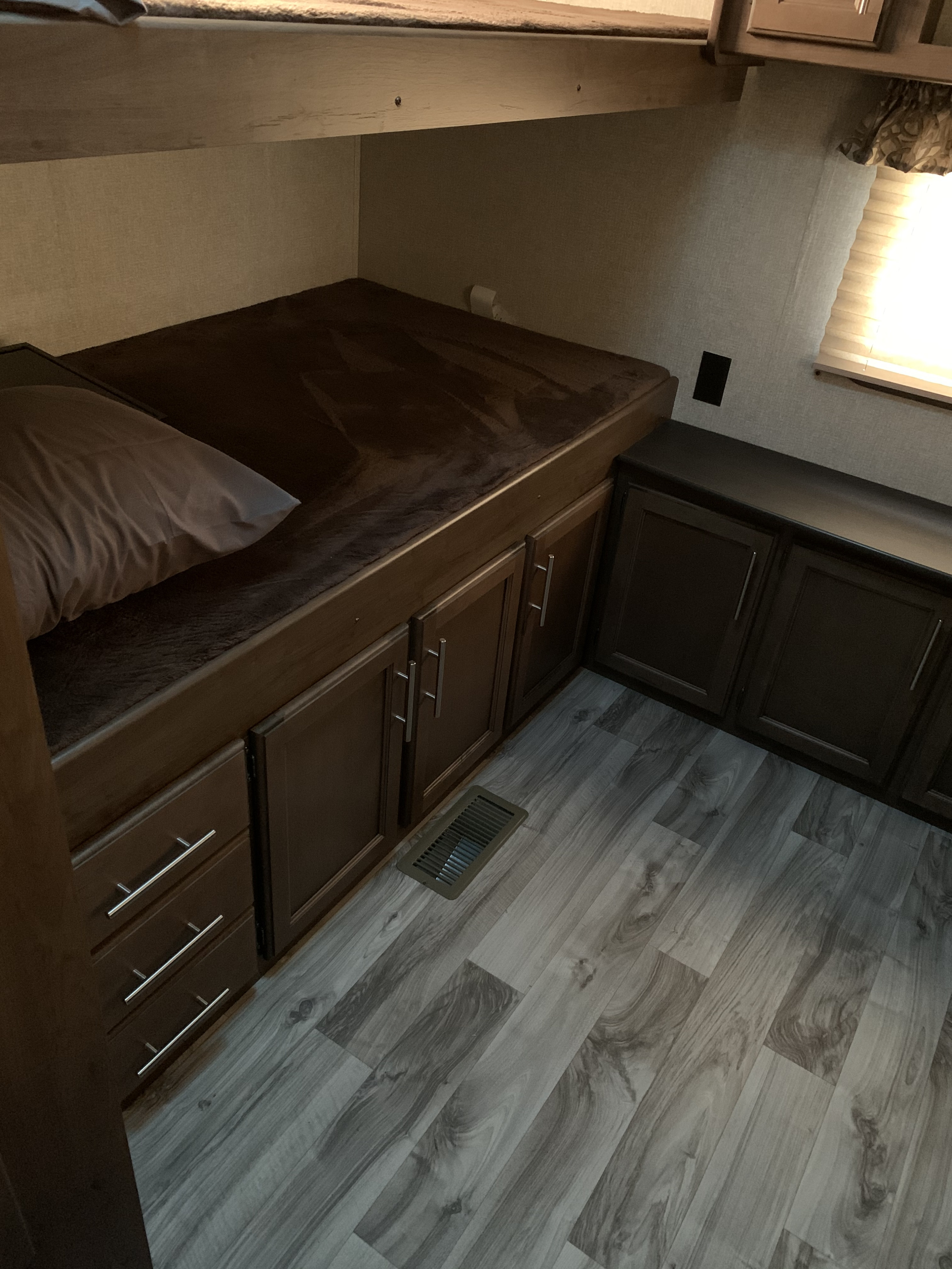 RV rental interior: A lower bunk bed with a brown mattress & pillow, built-in wood cabinets and drawers, plus light flooring.. Keystone RV Cougar 2019