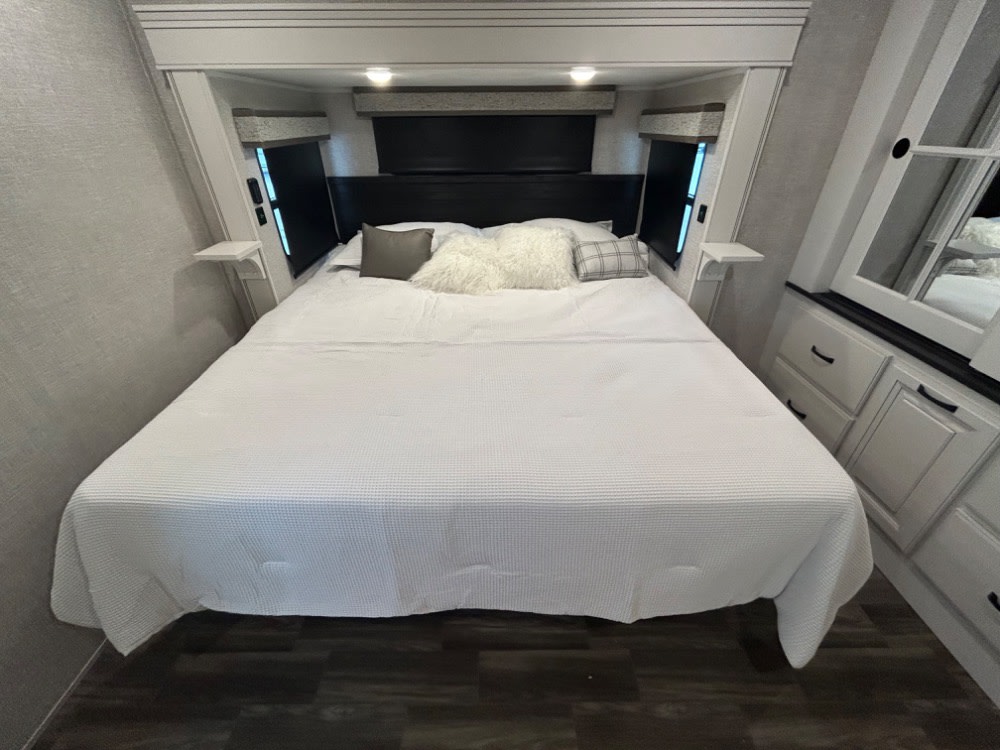 Spacious RV rental bedroom with a large white bed, integrated storage, and soft overhead lighting.. Jayco North Point 2025