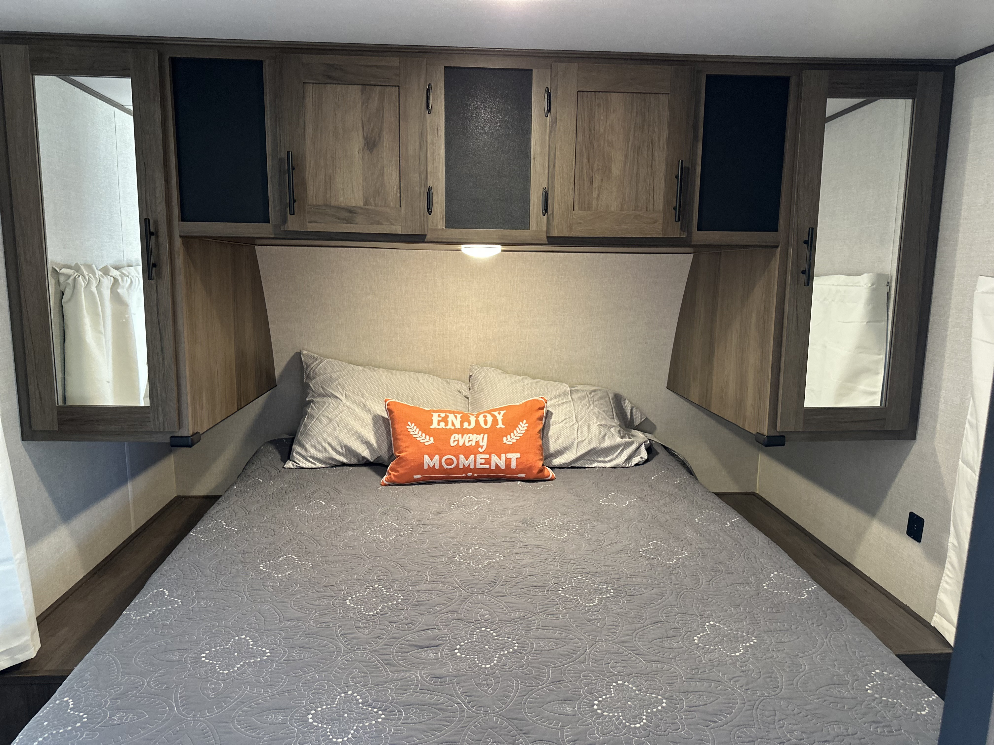 Inside a cozy RV rental bedroom: a comfy bed with patterned bedding, a vibrant accent pillow, and ample overhead storage.. Prime Time Avenger 27 DBS 2021