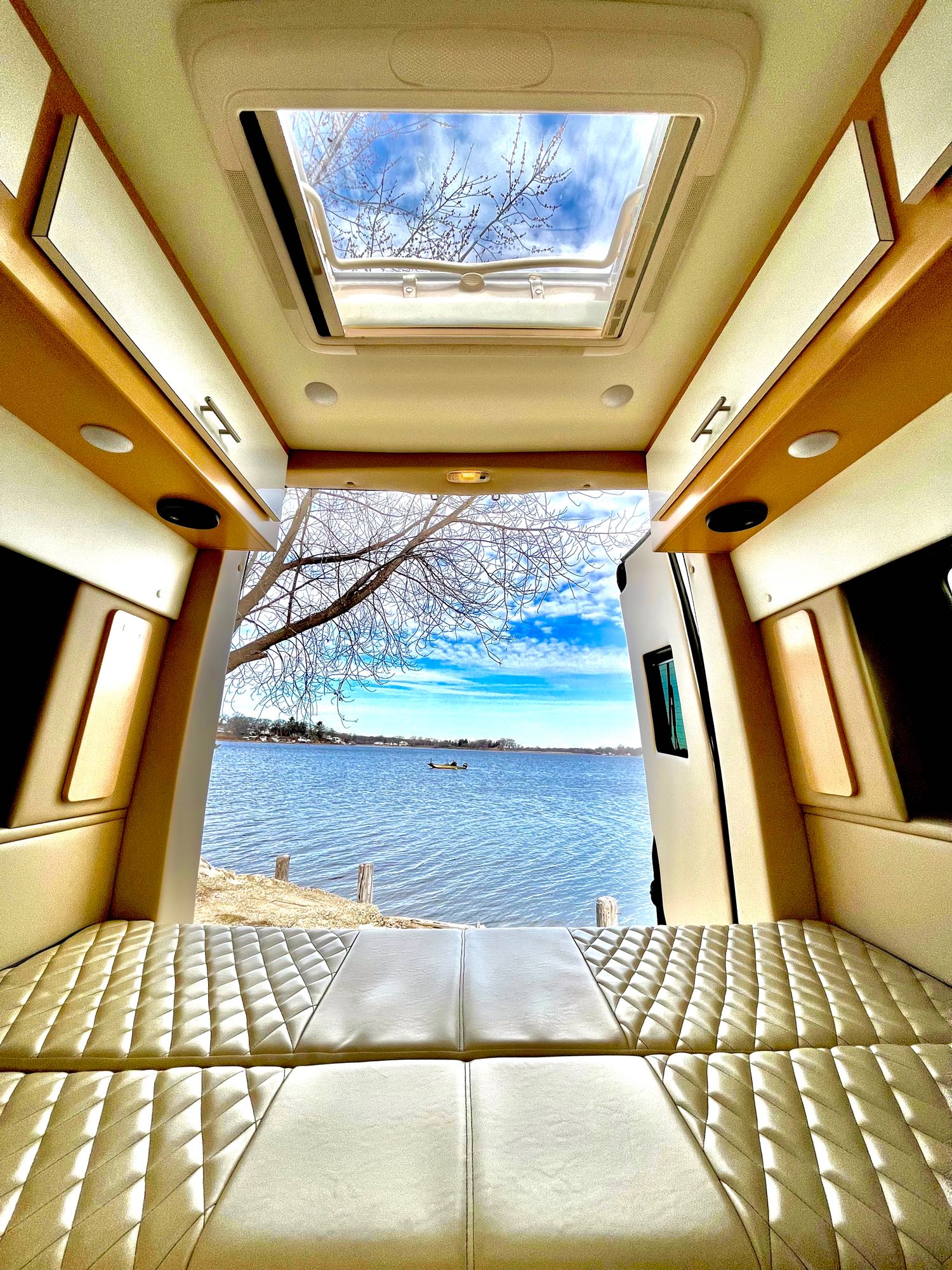 Inside an RV rental: quilted bed, open doors to a serene lake view and blue sky. Perfect for van life adventures.. Regency Xalta 2022