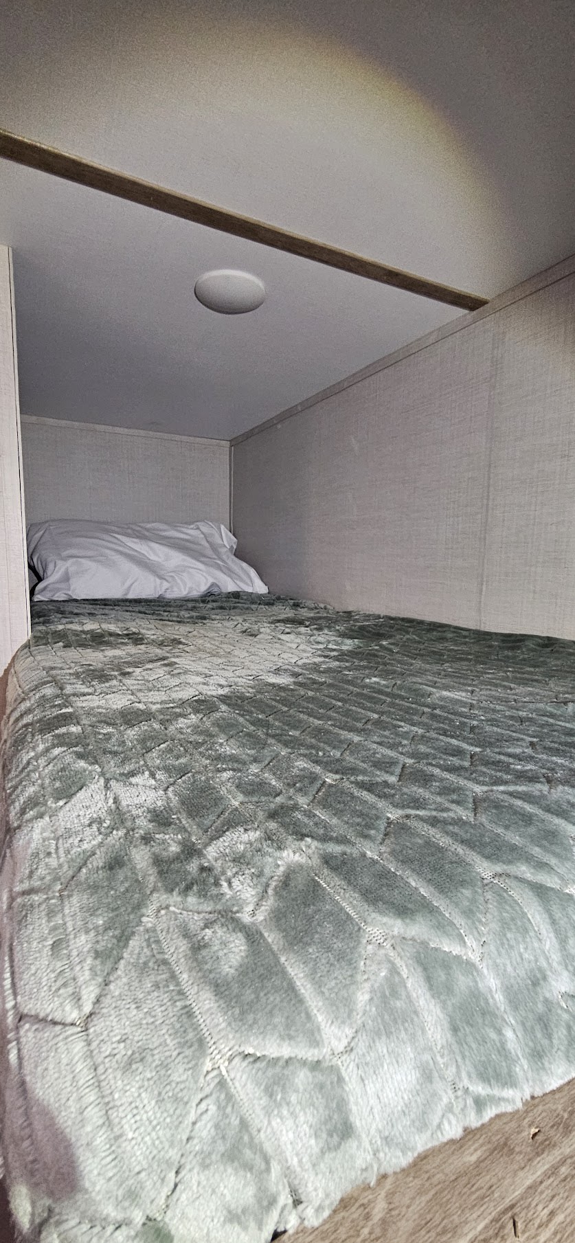 Cozy RV rental bunk bed with a quilted green blanket and pillow, ideal for a compact sleeping space.. Gulf Stream Ameri-Lite LE 2023