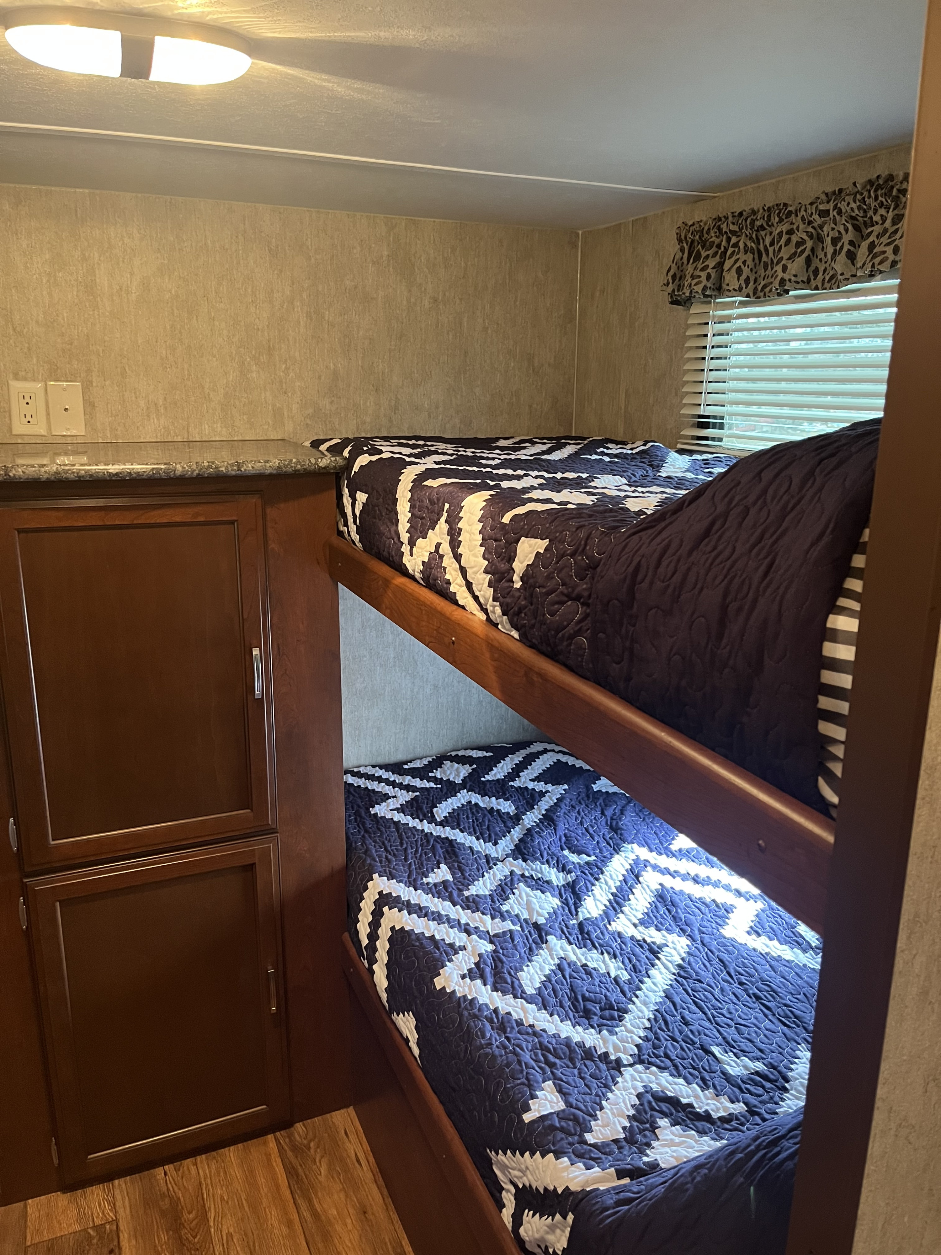 Inside an RV rental: two bunk beds with patterned quilts, wooden cabinets, and a window.. Keystone RV Passport Grand Touring 2015