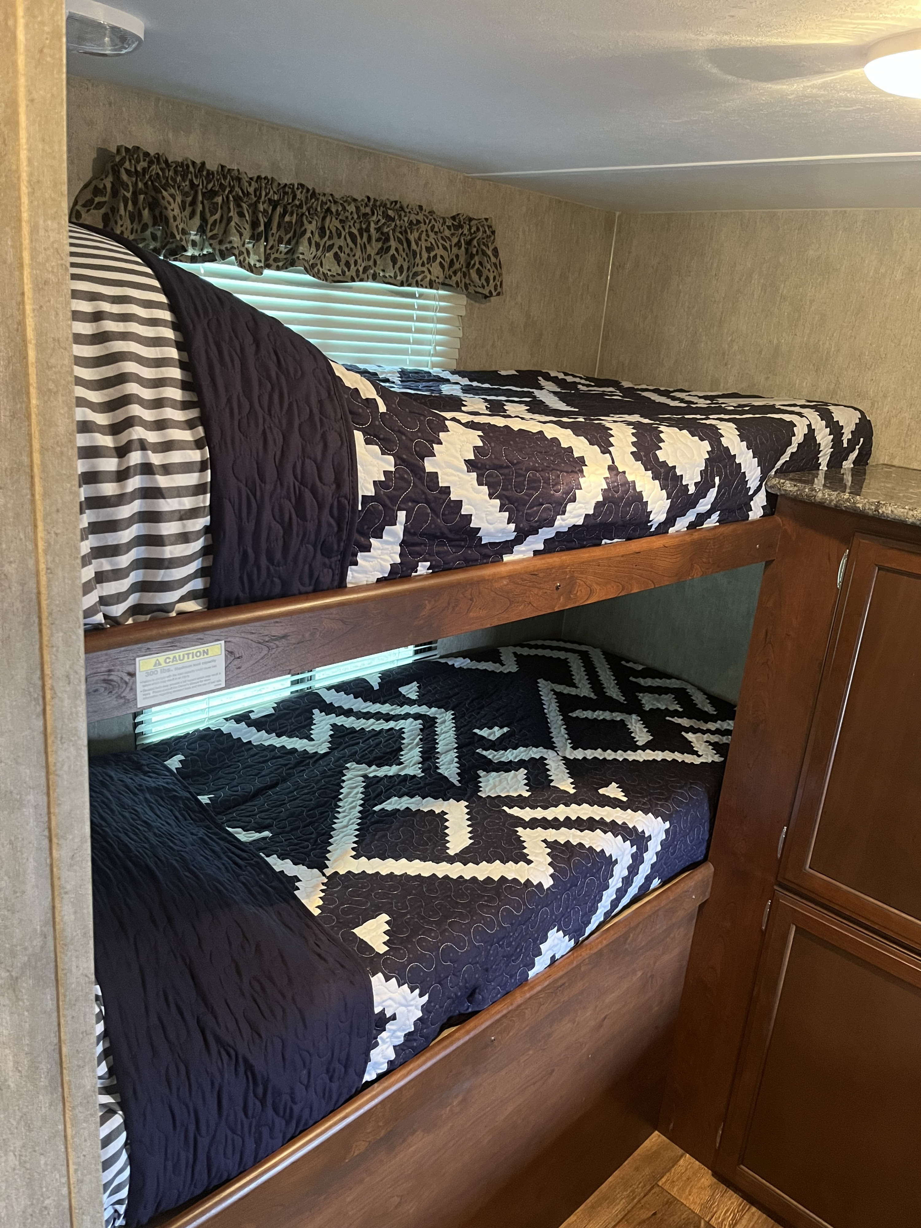 Cozy bunk beds in an RV rental, featuring navy and white geometric patterned quilts. Perfect for family adventures.. Keystone RV Passport Grand Touring 2015