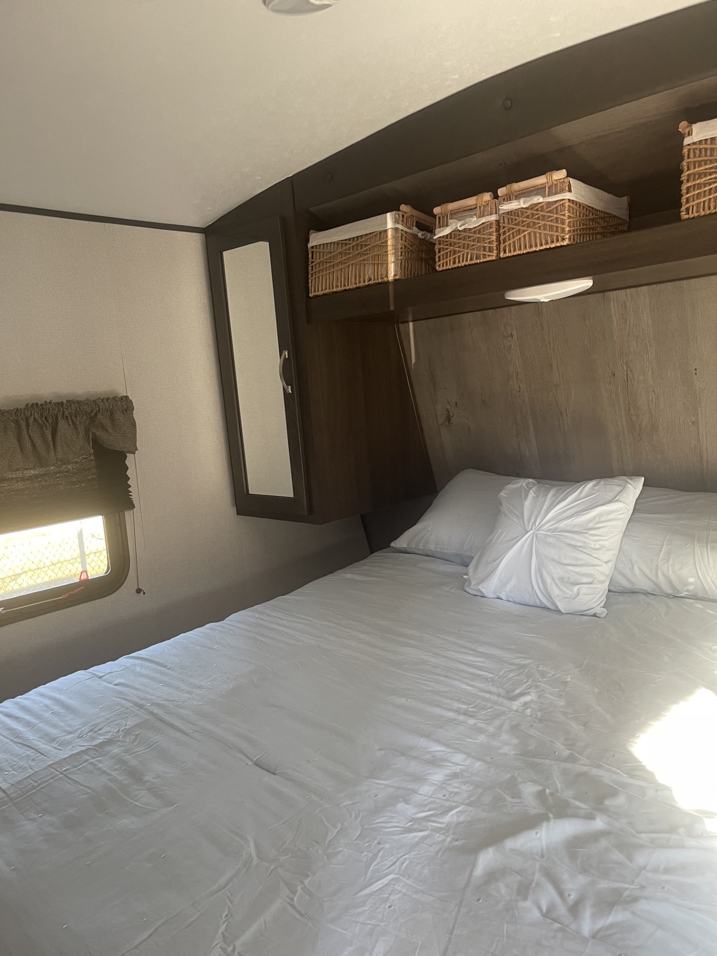 RV rental bedroom interior: Features a large bed with white linens, overhead storage with woven baskets, and a window.. Keystone RV Springdale 2020