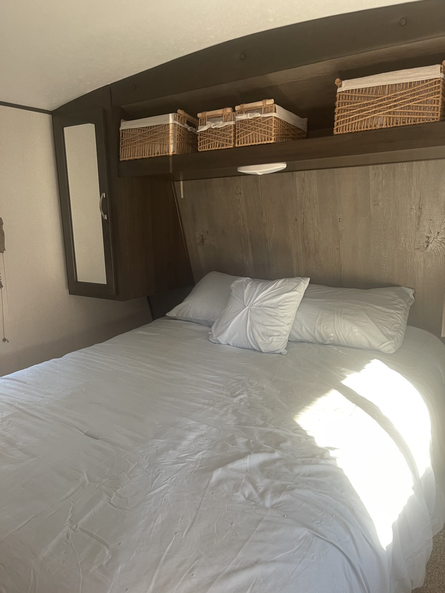 Inside an RV rental, this bright bedroom offers a cozy bed with white linens and woven storage baskets overhead.. Keystone RV Springdale 2020