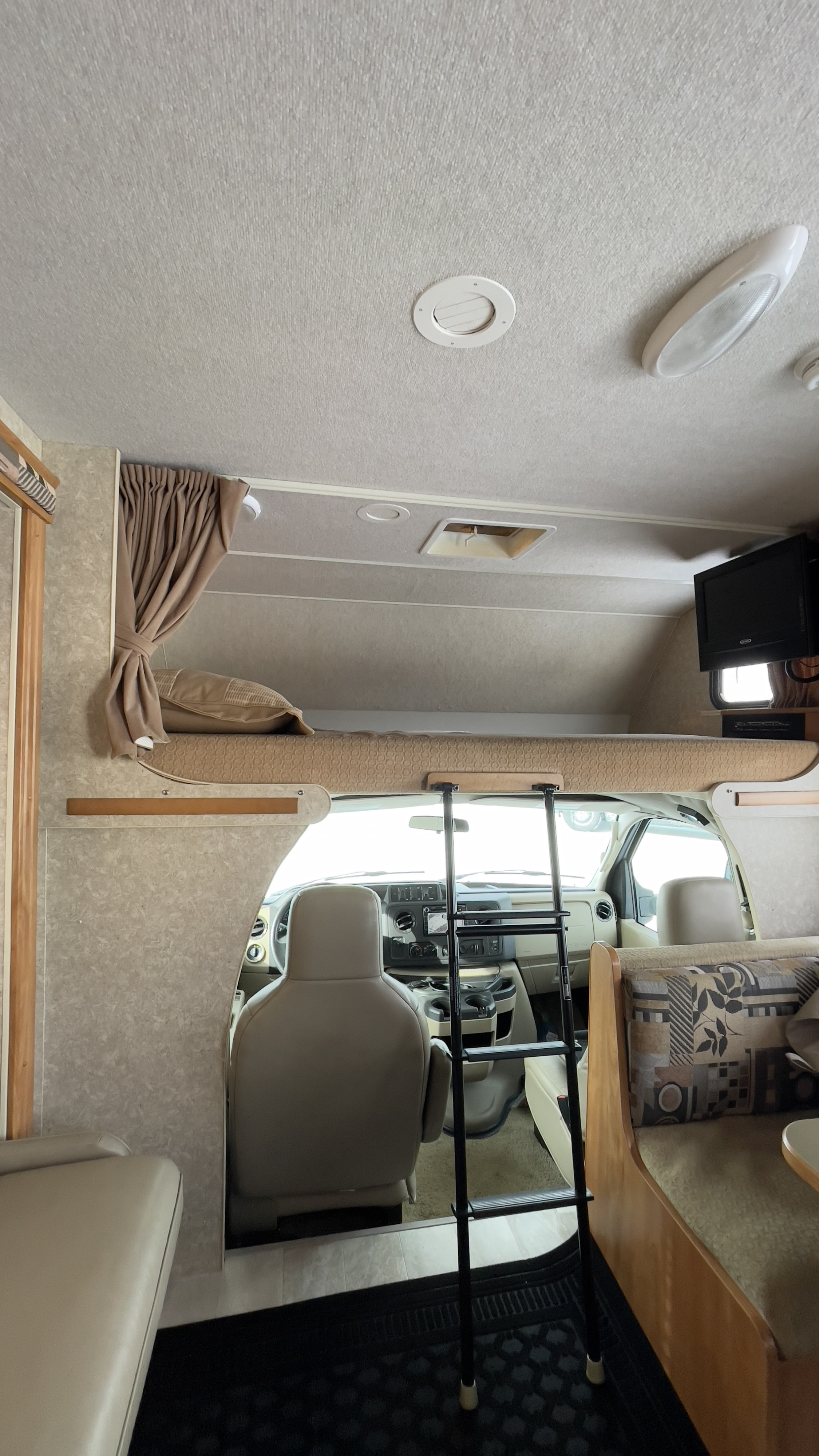 Spacious RV rental interior featuring a cozy cab-over bunk with ladder, cockpit, and dinette seating. Perfect for your next adventure.. Winnebago Access 2010