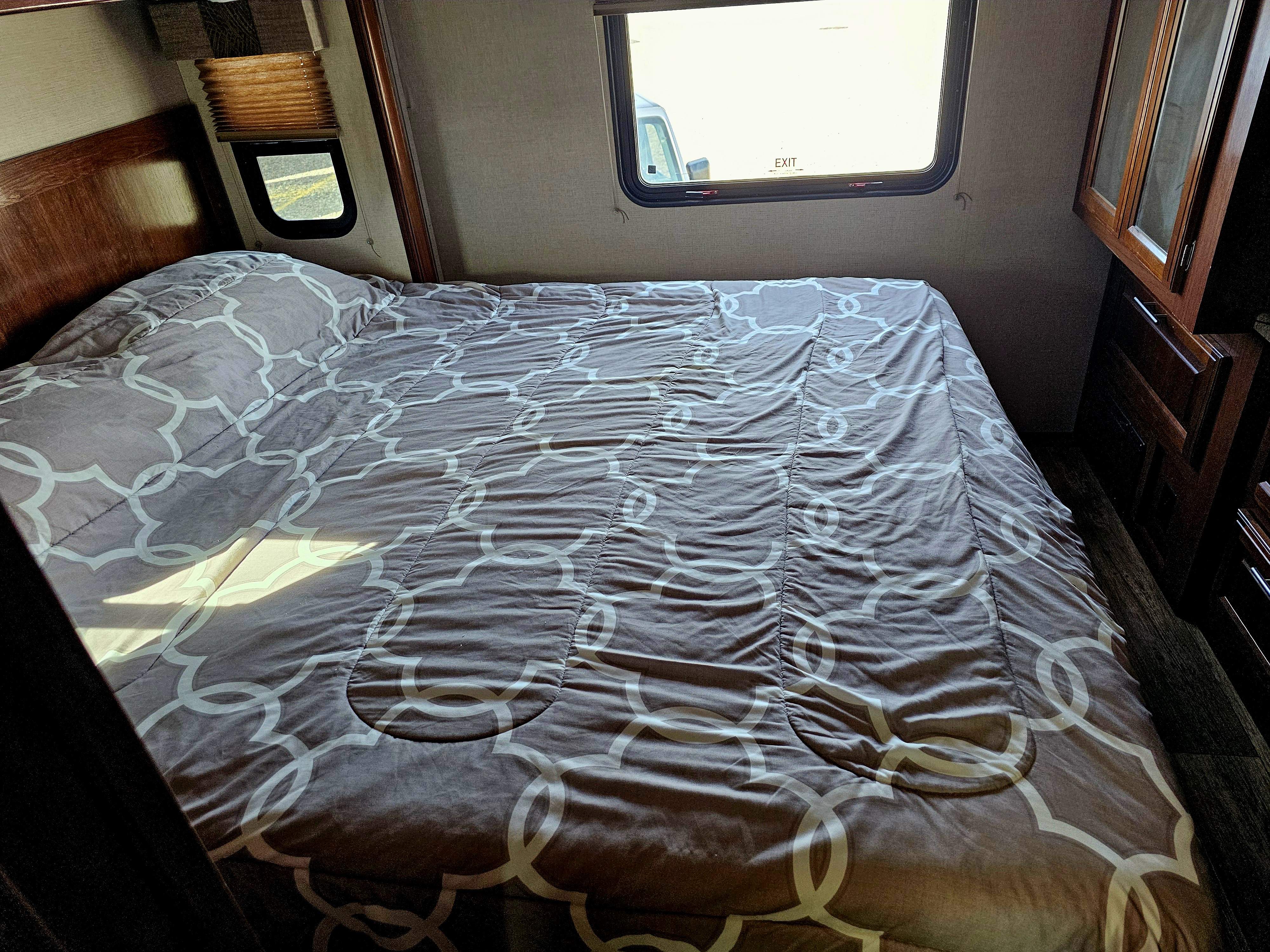 An RV rental bedroom shows a bed with a patterned comforter, windows with sunlight, and wooden storage.. Forest River FR3 30DS 2017
