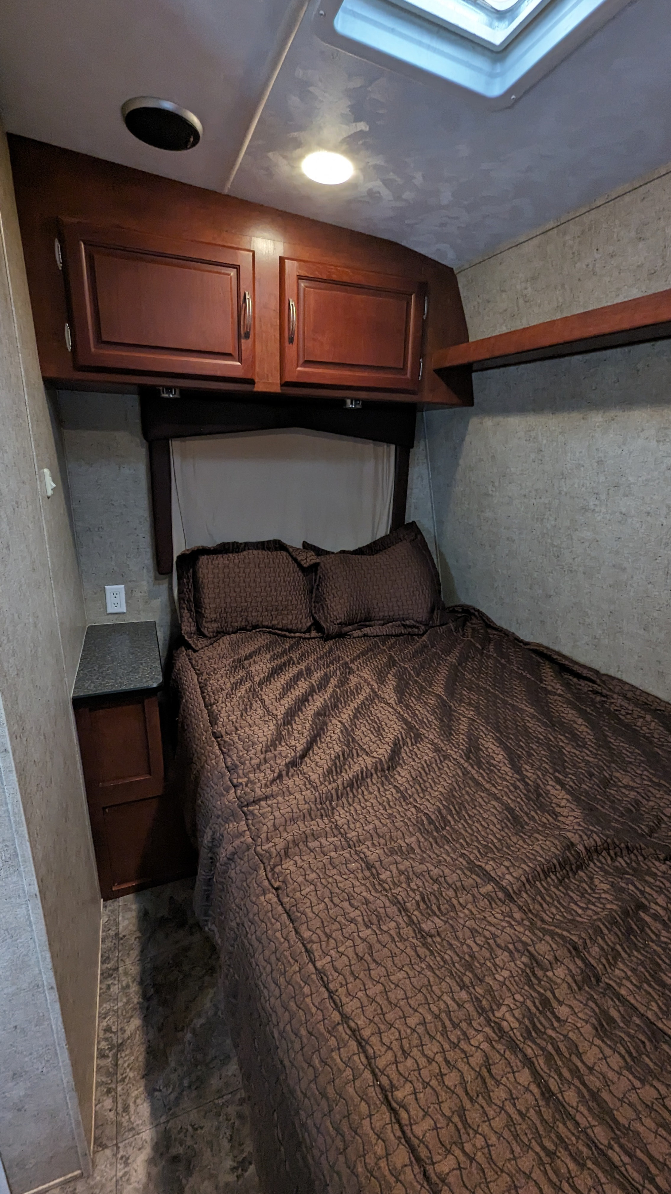 RV rental: Cozy bedroom interior with a queen bed, dark wood storage cabinets, bedside table, and overhead skylight.. Forest River Sandstorm 2010