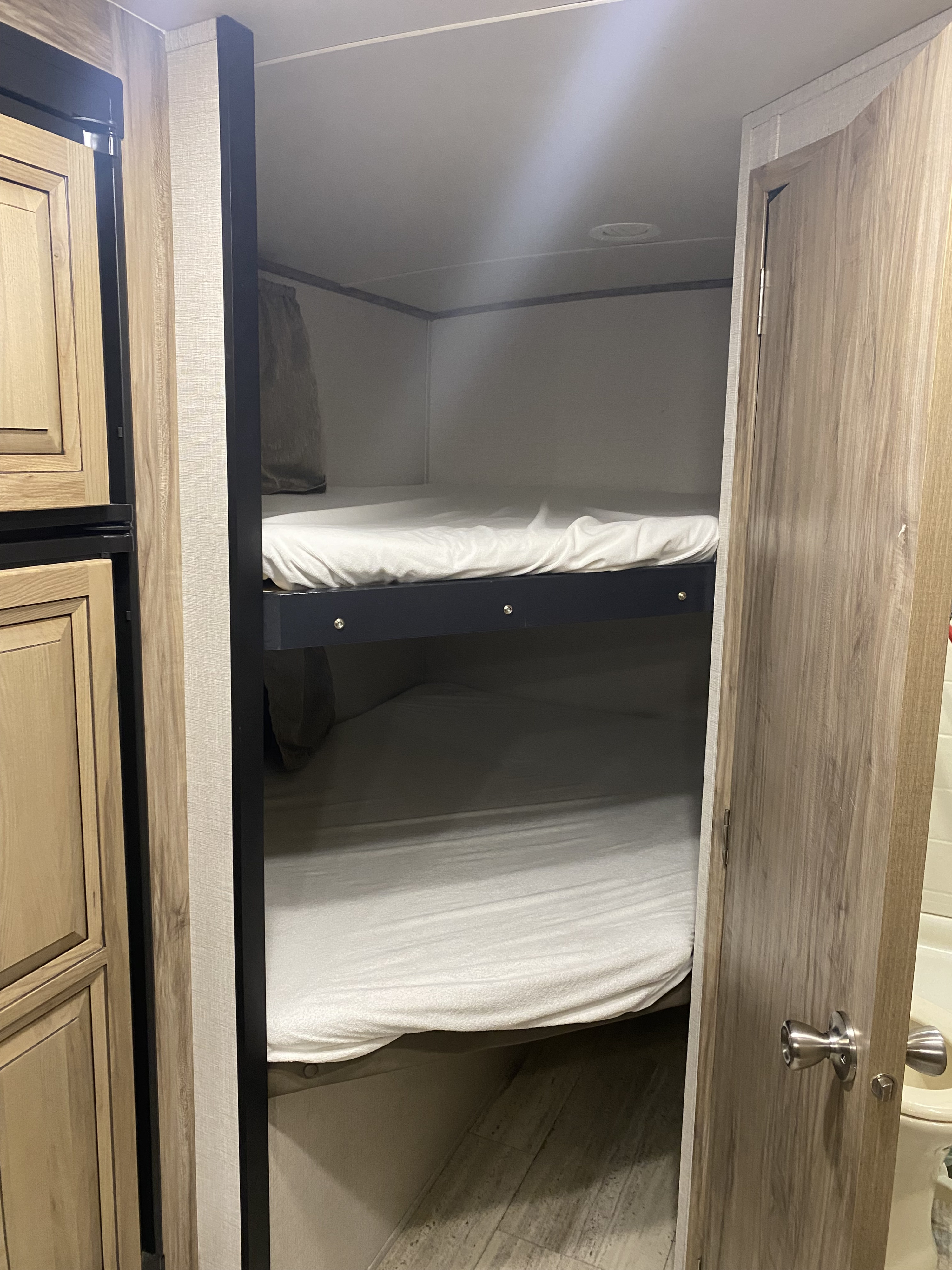 Inside an RV rental, showing neat bunk beds with white sheets, adjacent to wood-paneled cabinets and a door.. Palomino 240bhs 2018