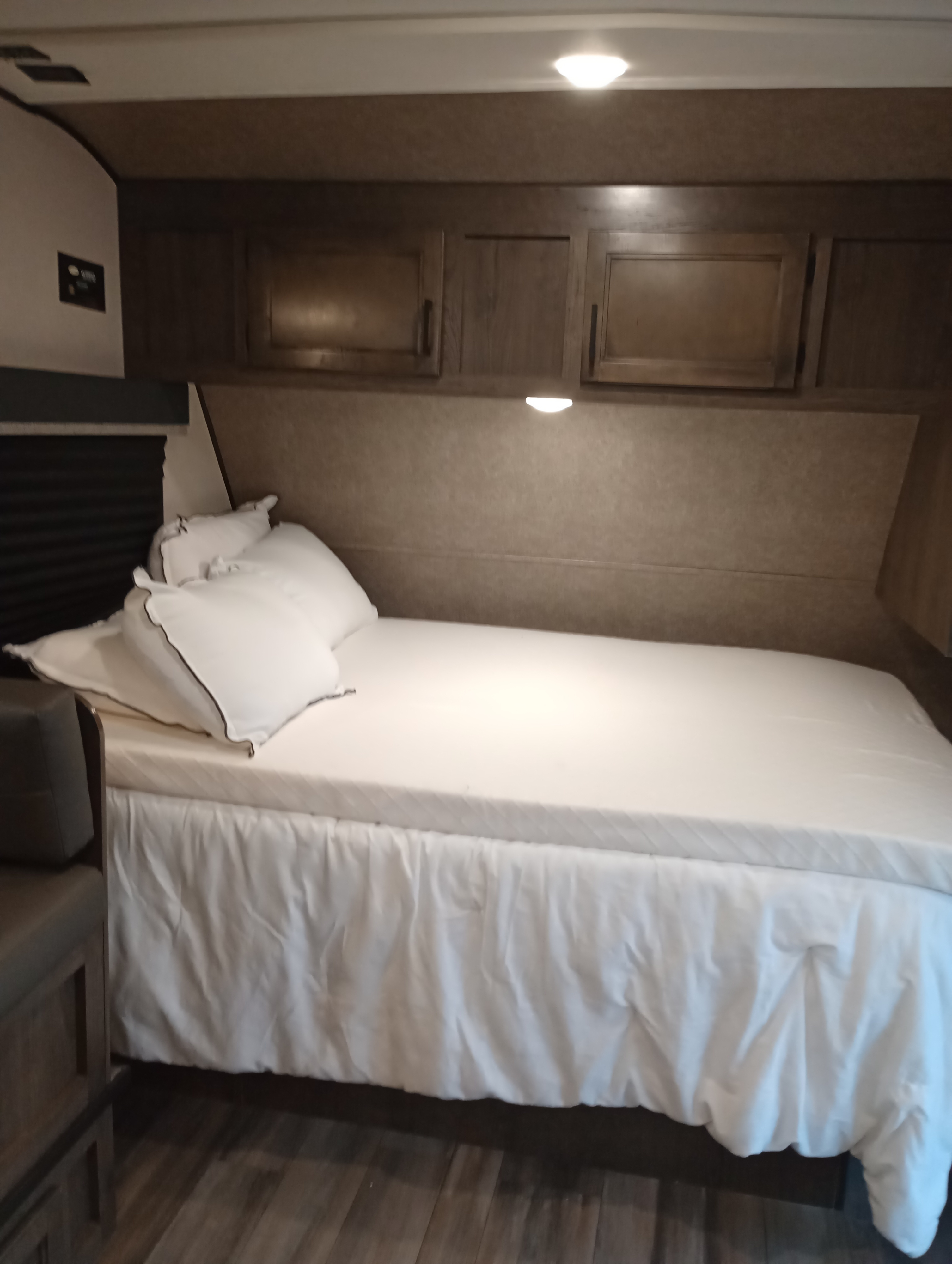 RV rental bedroom with a comfy bed, white bedding, overhead cabinets, and wood-look flooring.. Highland Ridge RV Open Range 2022