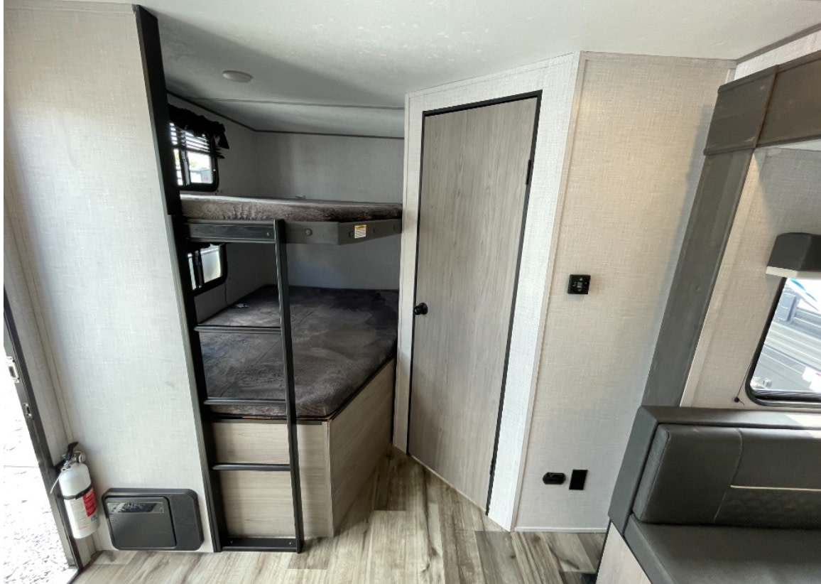 RV rental interior features bunk beds, a door, and a fire extinguisher. Light-toned walls and wood-look flooring.. Dutchmen Coleman Light 2023