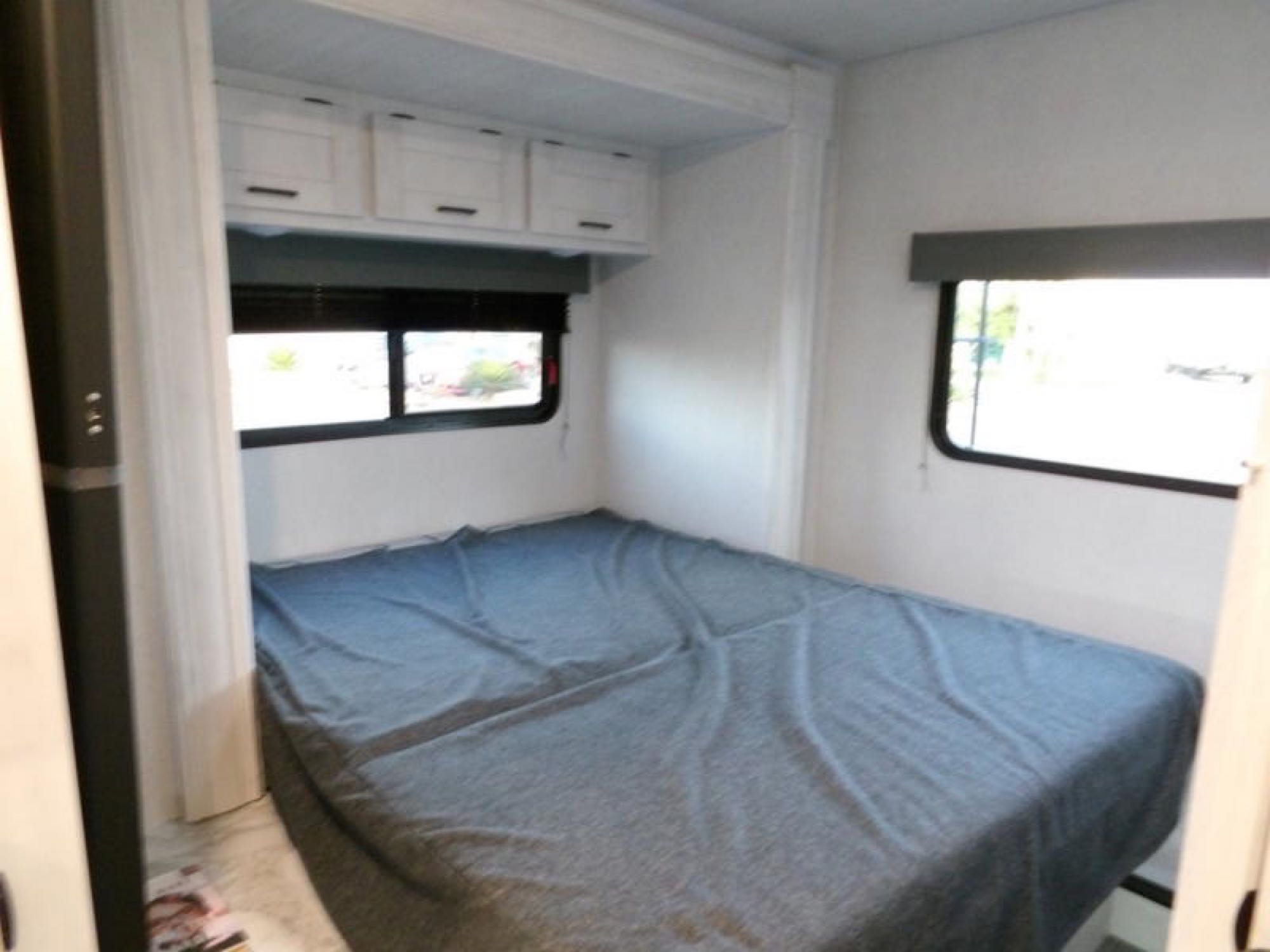 Inside an RV rental: a compact bedroom featuring a bed with a blue cover, side windows, and white overhead storage.. Forest River Entrada 2600DSF 2024