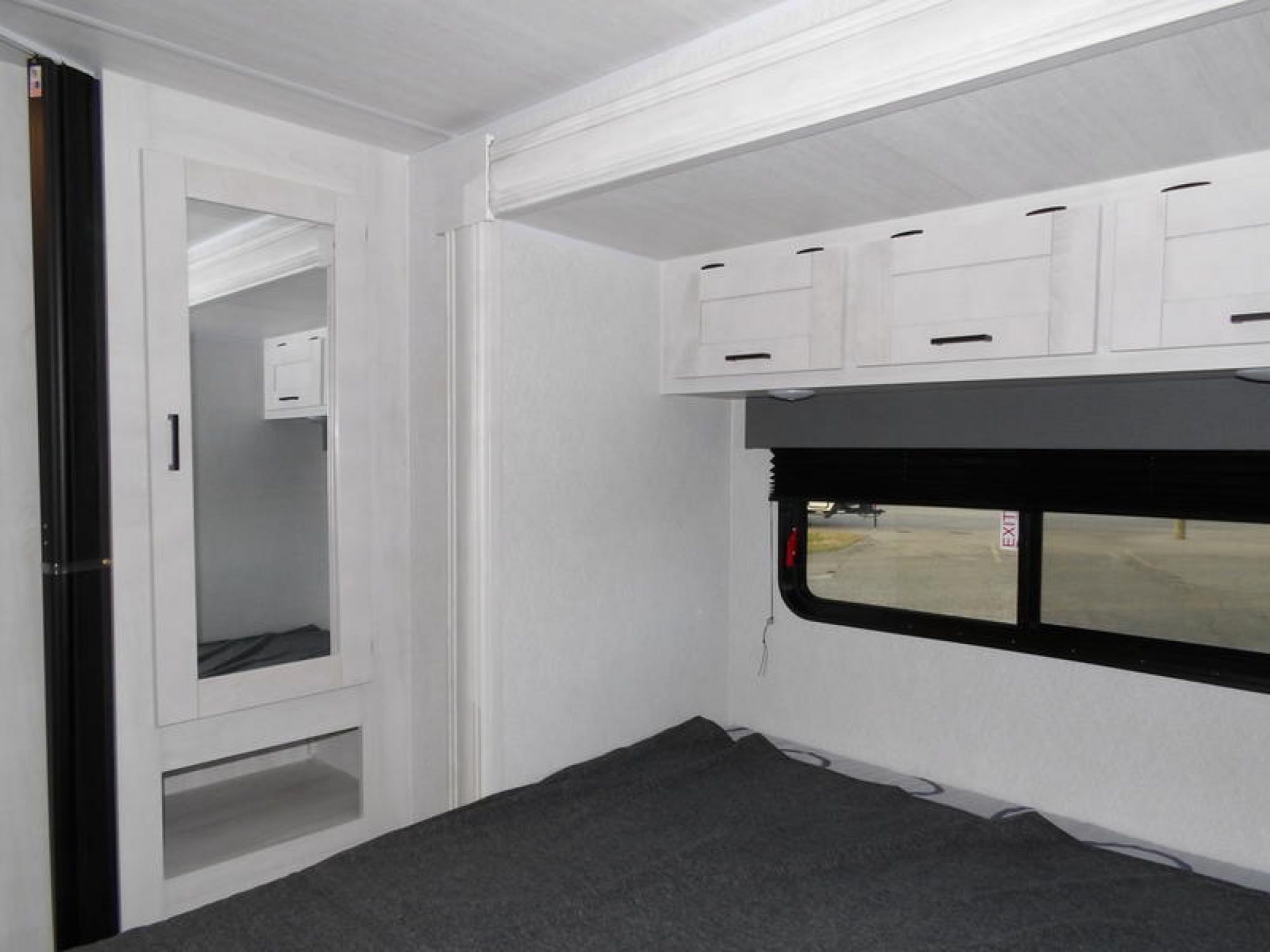 A cozy RV rental bedroom interior with a dark grey bed, overhead storage, and a mirrored wardrobe on the left.. Forest River Entrada 2600DSF 2024