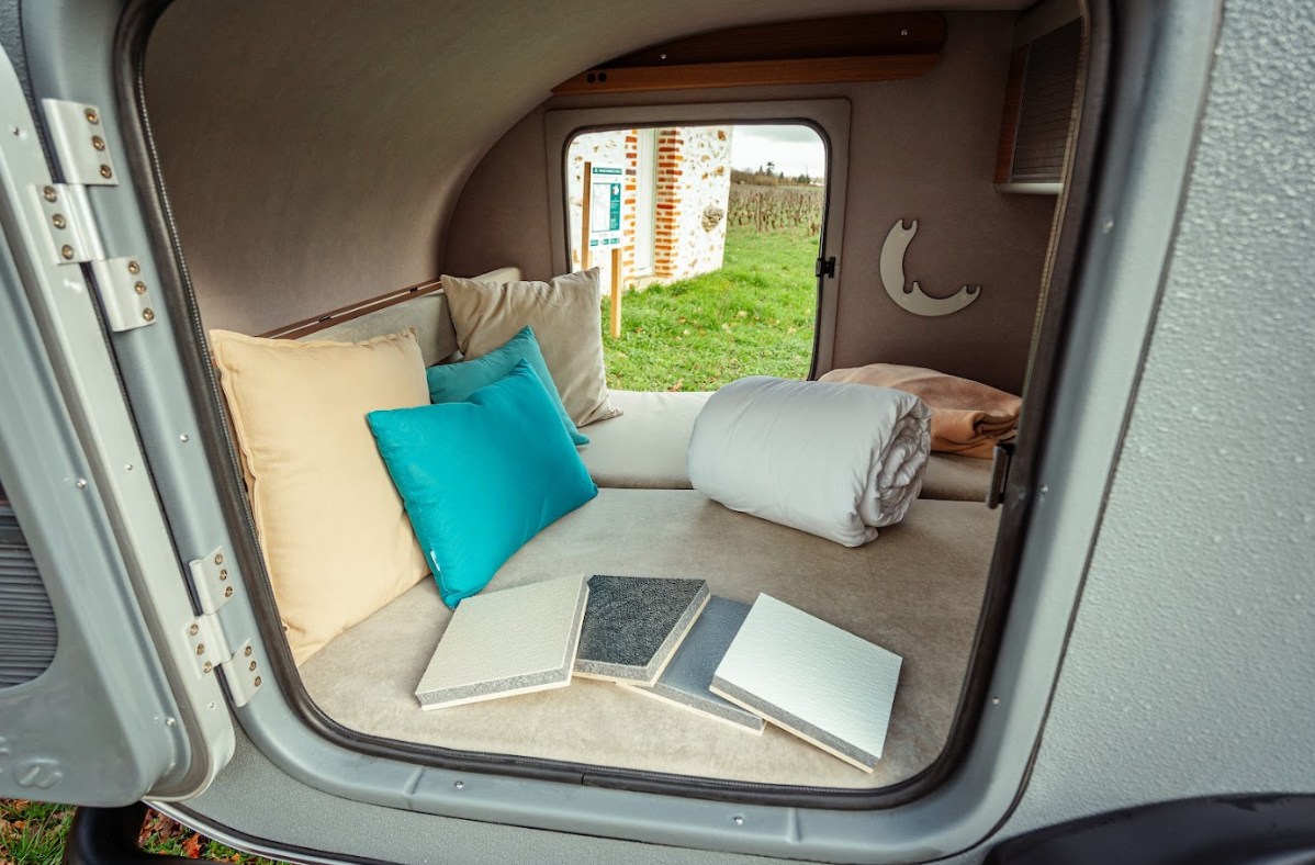 Step inside this cozy RV rental camper, featuring a comfortable bed, accent pillows, material samples, and a tranquil vineyard view.. Caretta 1500 2024