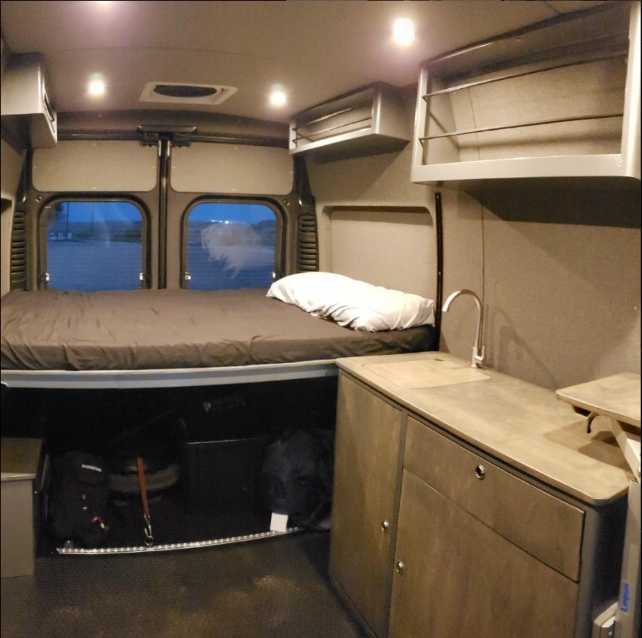 Explore this RV rental's interior: elevated bed, ample storage, and a kitchenette. Ideal for a camper van adventure.. Dodge Sprinter Van 2021