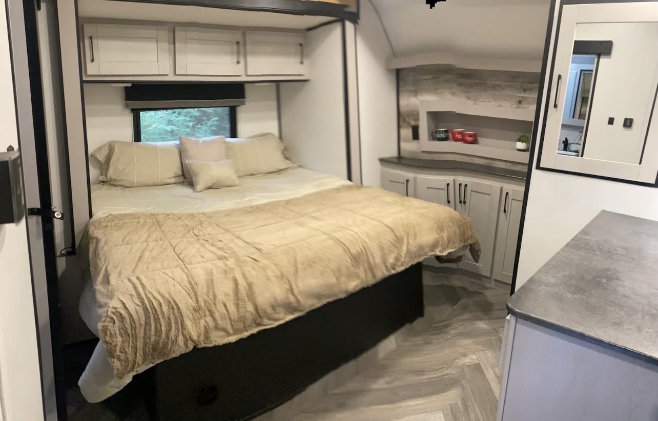 Modern RV rental bedroom with a comfy bed, overhead storage, and a built-in counter with decorative shelf.. Heartland Torque 2022