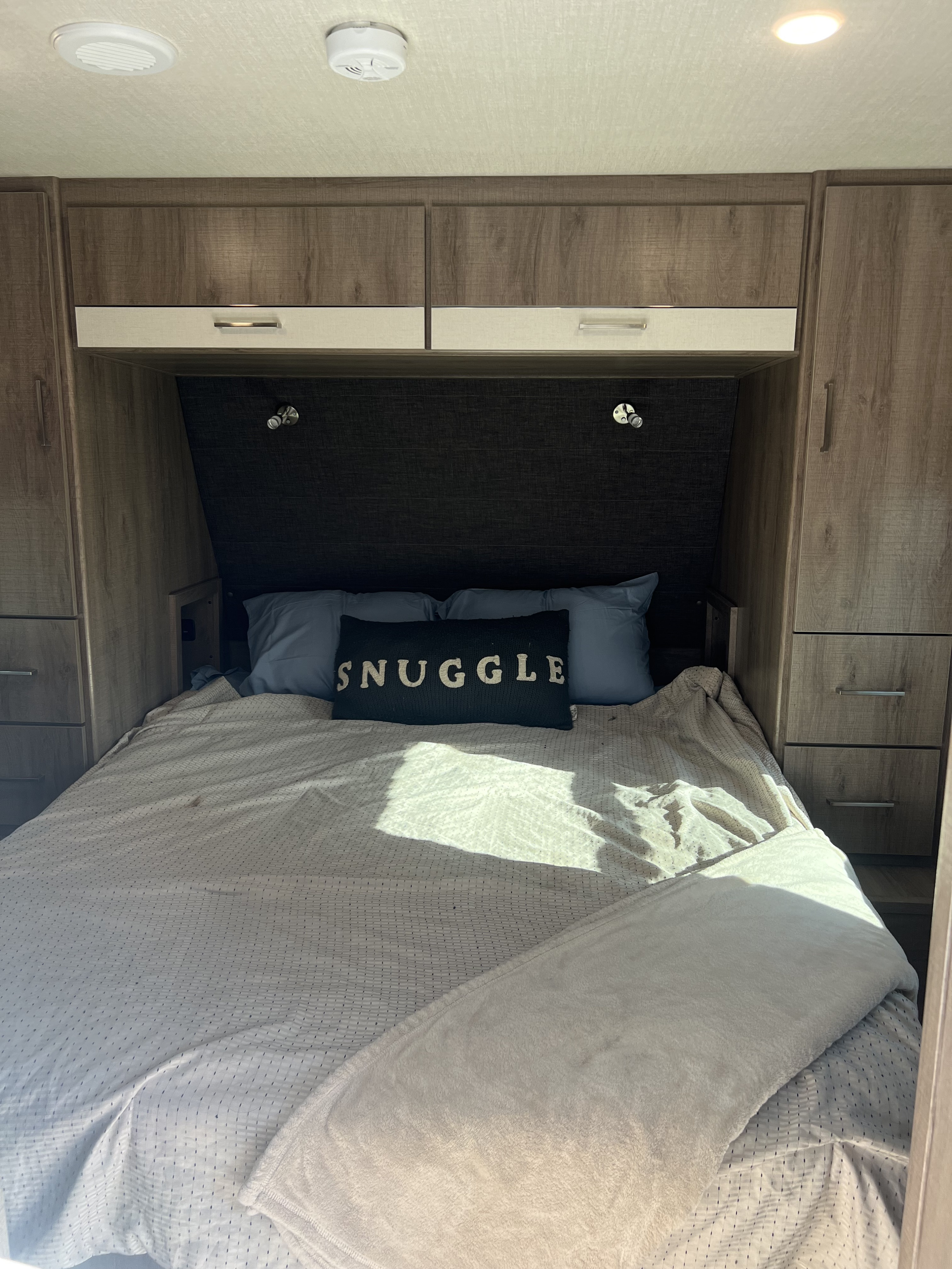 Inside an RV rental: a cozy bedroom with a 'SNUGGLE' pillow, bed, and built-in storage. Ideal for comfortable travel.. Grand Design Imagine XLS 2023