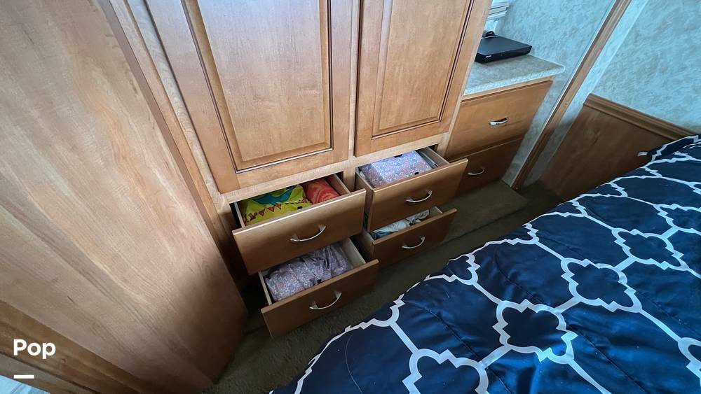 RV rental bedroom interior: light wood wardrobe & open drawers showing items, next to a patterned bed for travel comfort.. Winnebago Vista 2010