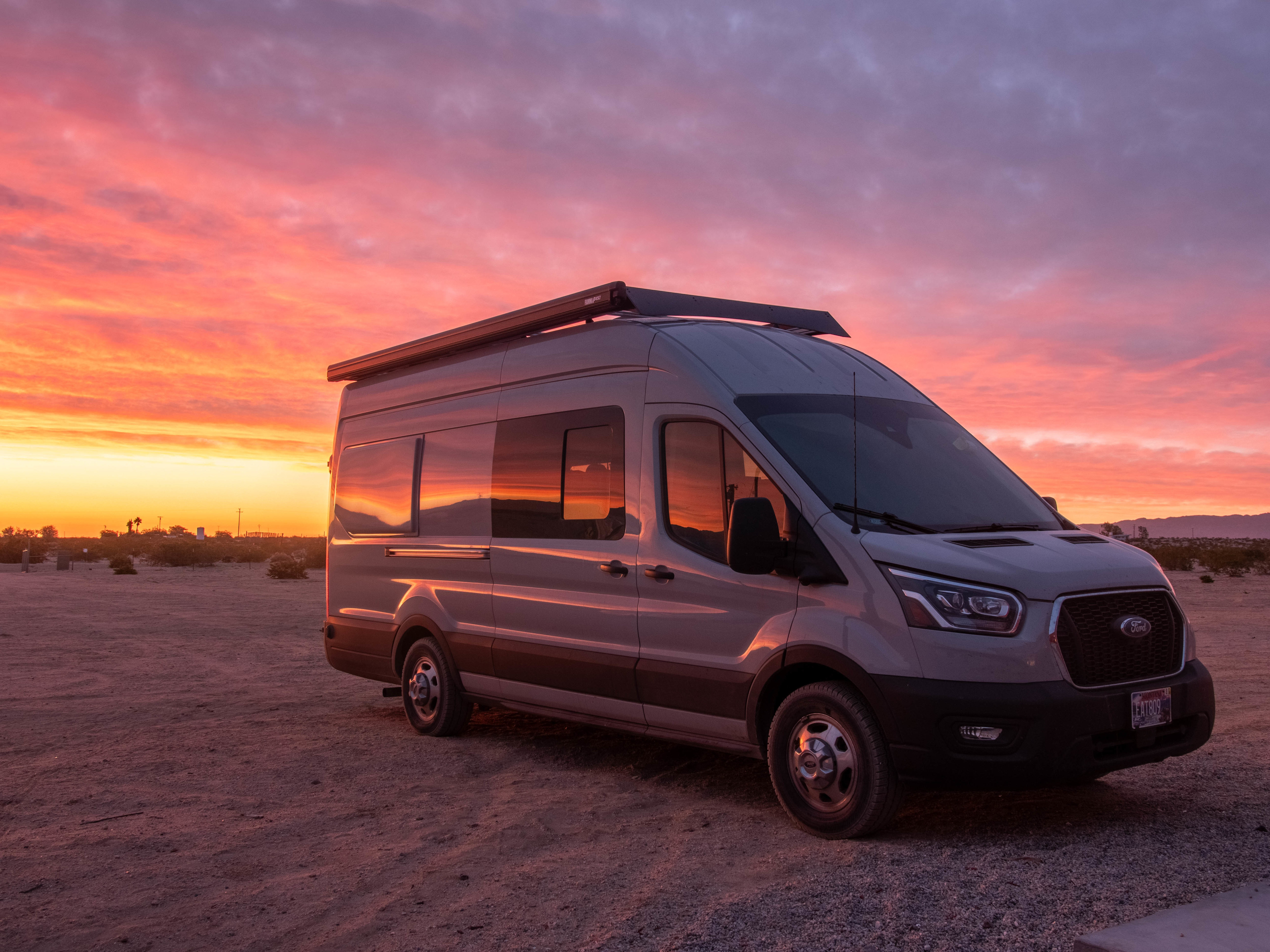An RV rental camper van bathed in the vibrant hues of a desert sunset. Perfect for adventure!. Ford Transit 2022