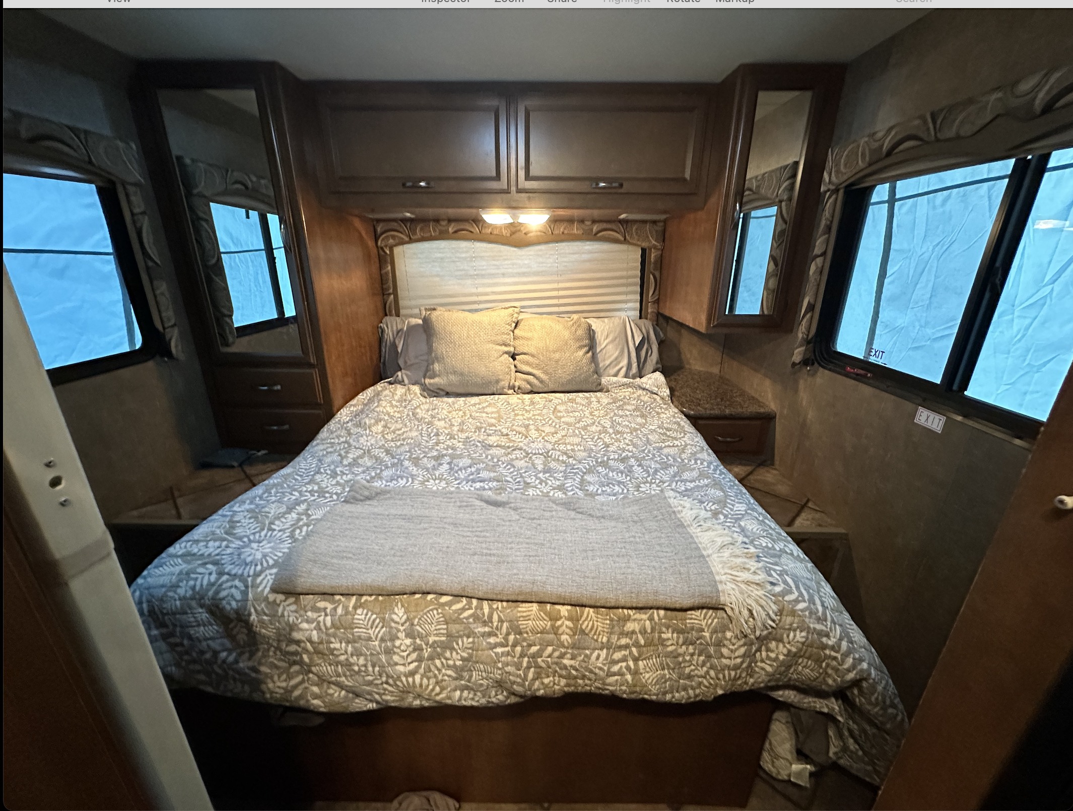 Cozy RV rental bedroom with patterned bedding, overhead cabinets, and dual windows. Ideal for comfortable journeys.. Thor Four Winds 2015