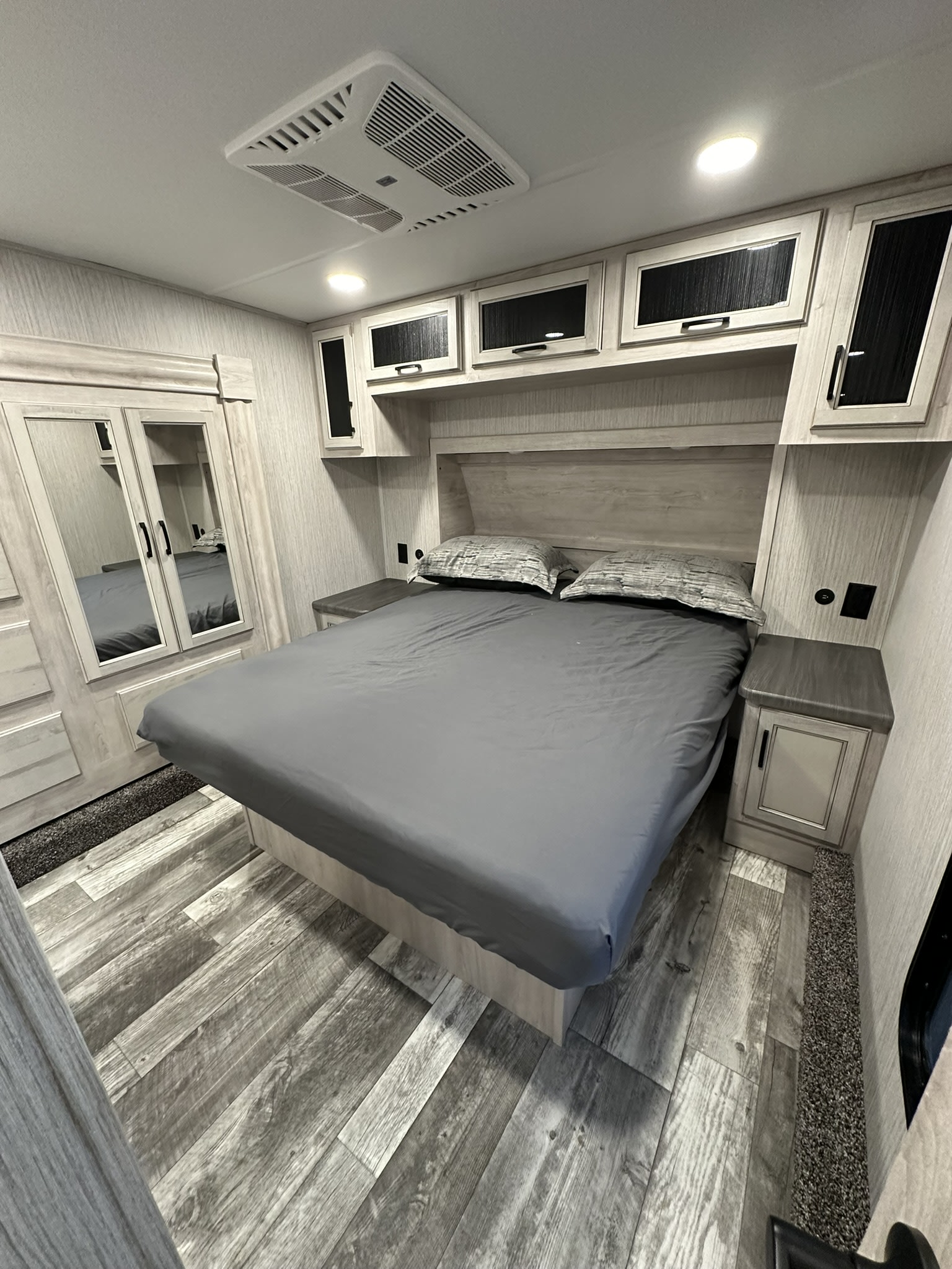 Spacious RV rental bedroom with queen bed, overhead cabinets, and mirrored wardrobe, ideal for comfortable travel.. Forest River Sierra 2022