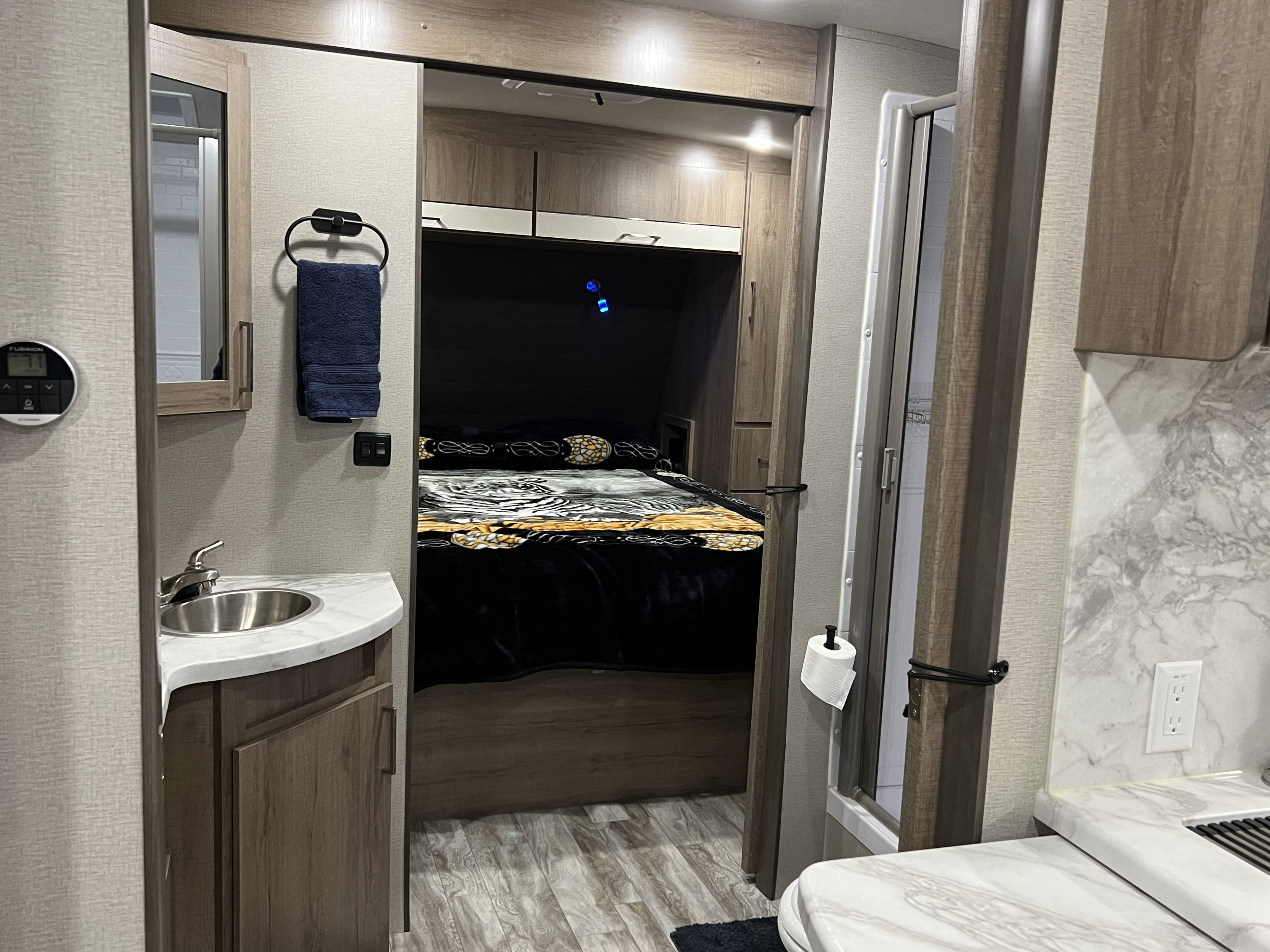 This rv rental features a compact, functional interior with a bathroom vanity, cozy bed, and shower, ideal for mobile living.. Grand Design 2910BH 2022