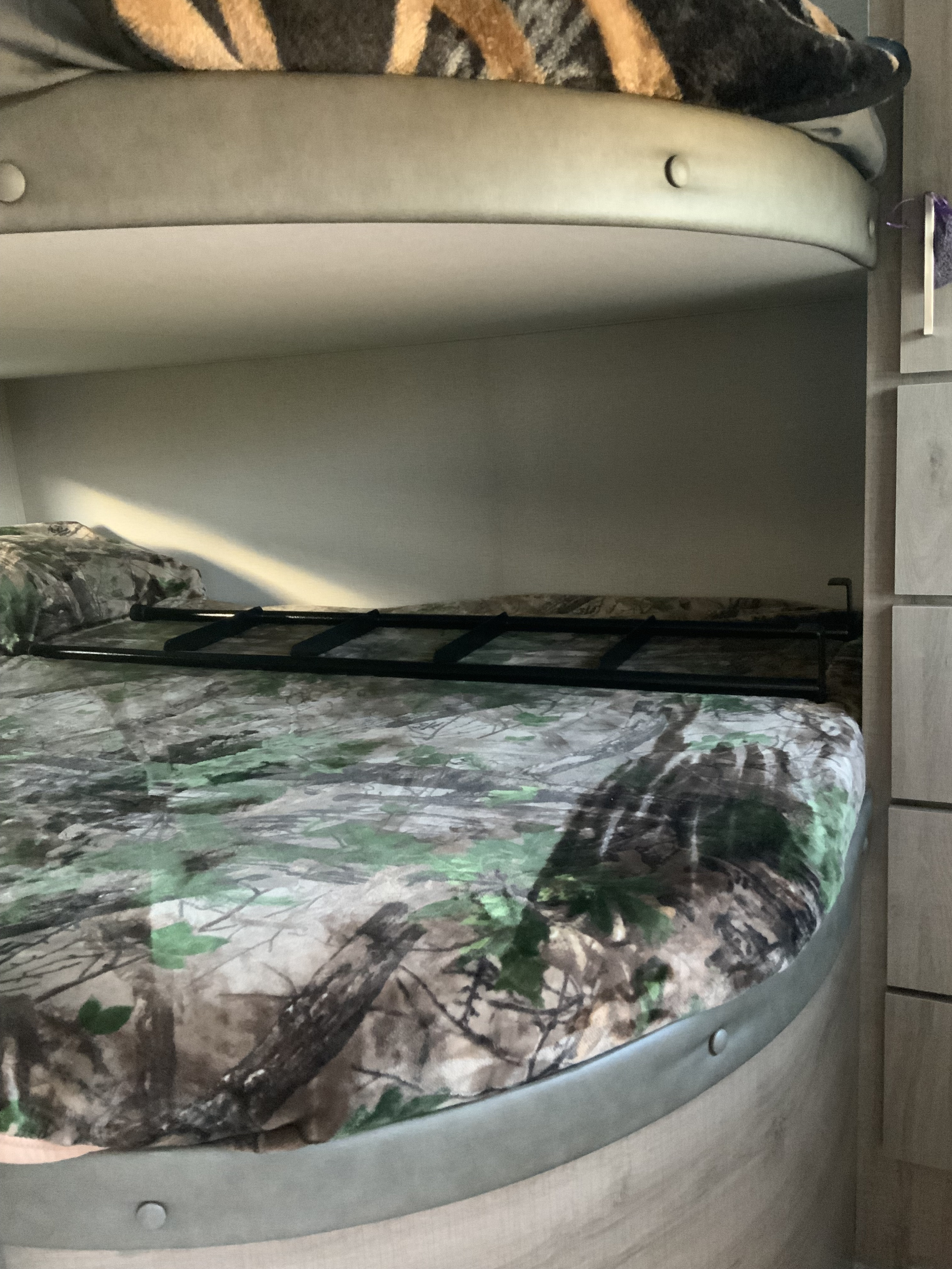 An RV rental's bunk beds, featuring a lower bunk with camouflage bedding, an upper bunk with a striped blanket, and a safety rail.. Grand Design 2910BH 2022