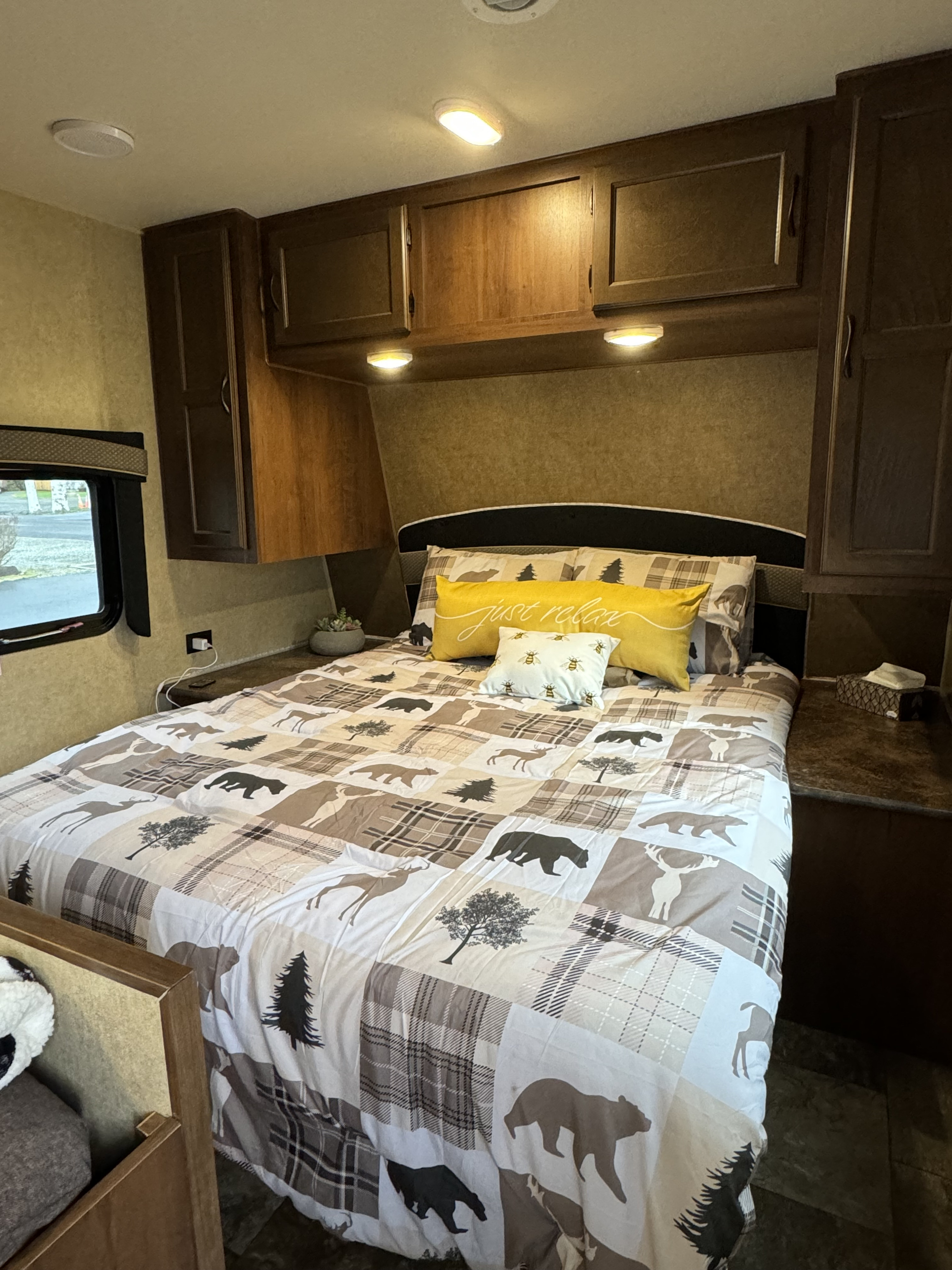 This RV rental bedroom offers a cozy bed with nature-themed bedding (bears, deer), overhead cabinets, and soft lighting for comfort.. Jayco Jay Flight 2014