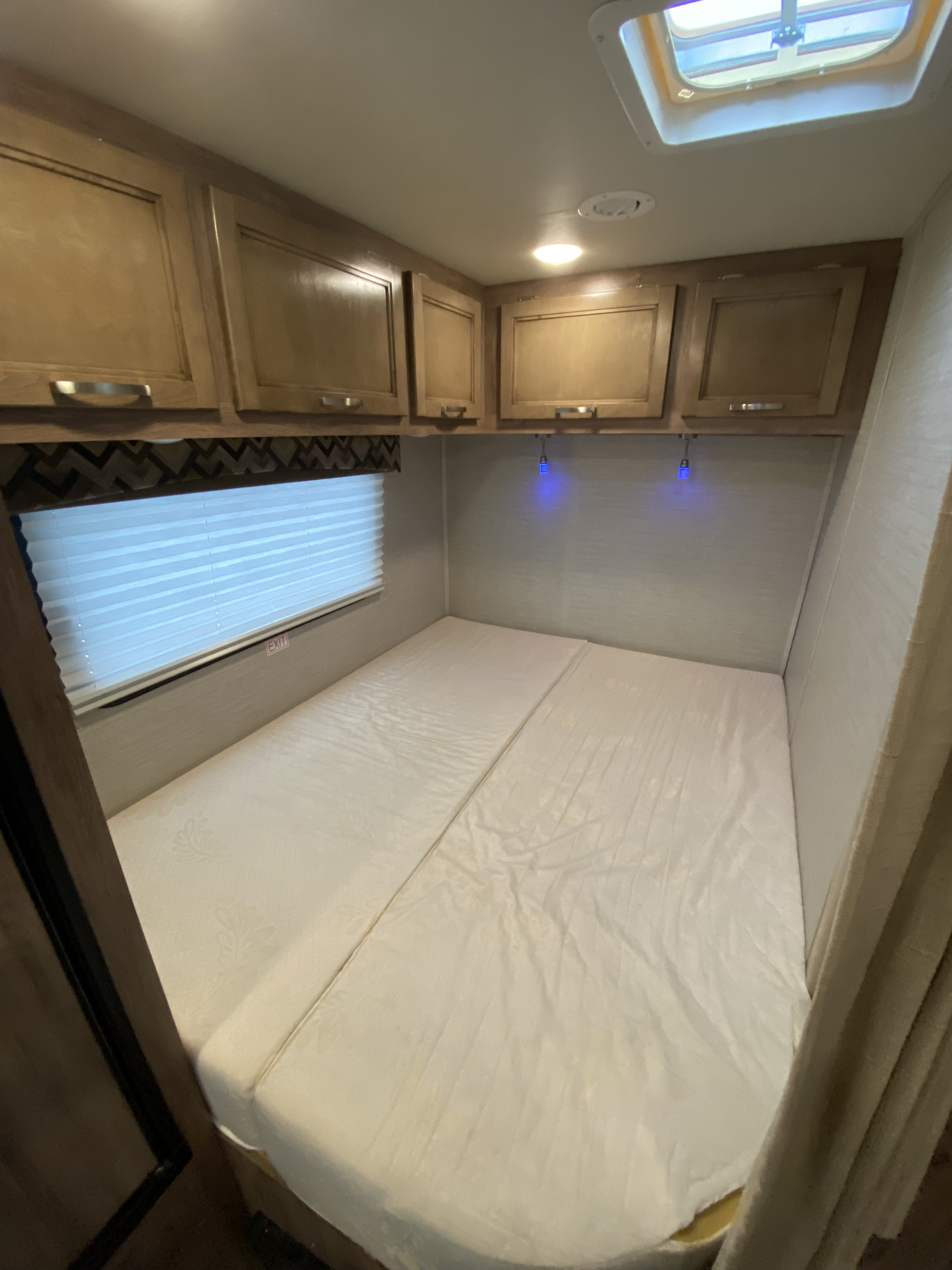 Cozy RV rental bedroom with comfortable bed, overhead cabinets, window, and skylight. Ideal for travel.. Jayco Redhawk SE 2019