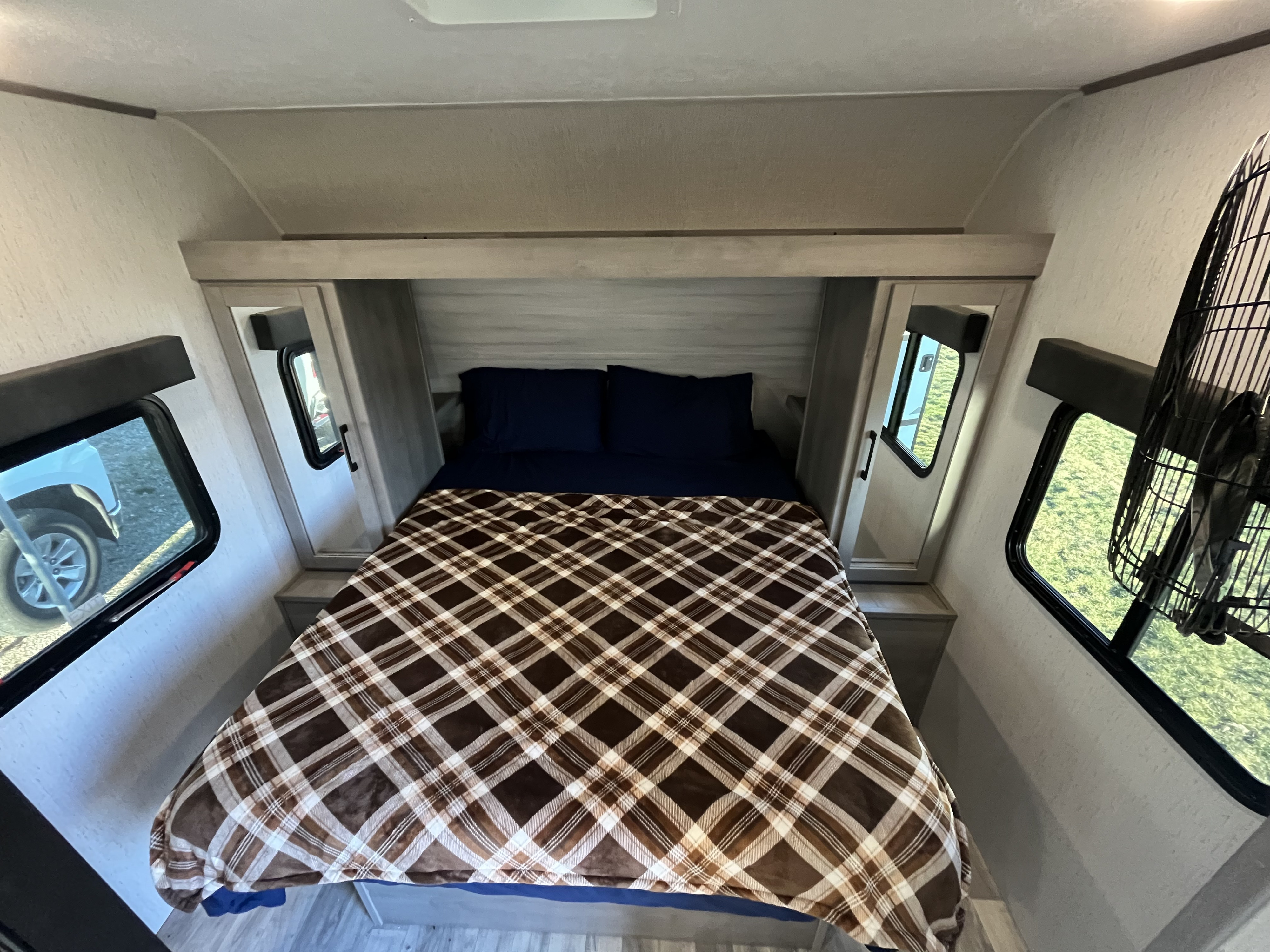 Cozy RV rental bedroom featuring a comfy plaid-covered bed, overhead cabinets, and windows revealing outdoor views.. Dutchmen Kodiak Bunk House 2019
