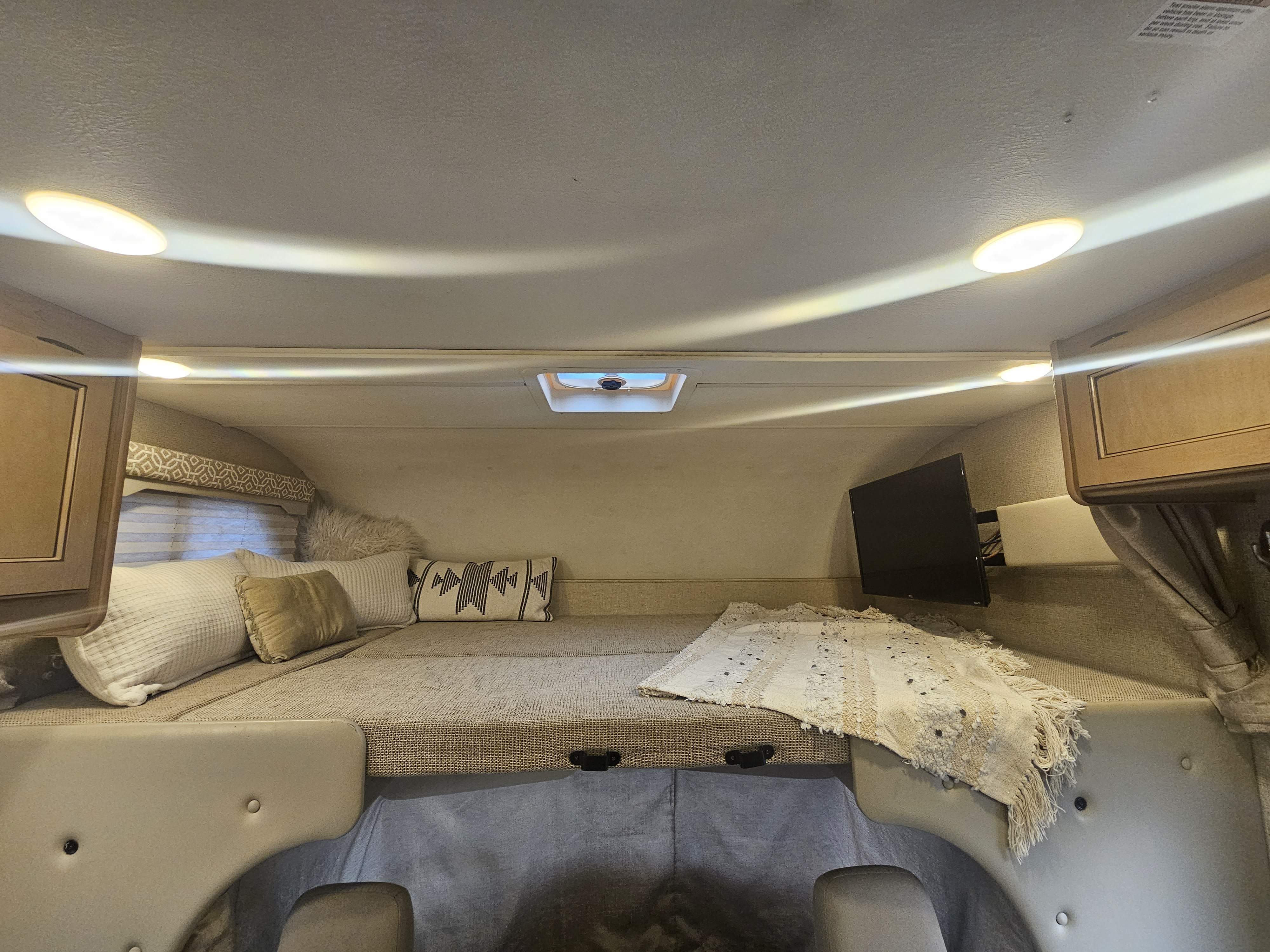 Cozy cab-over sleeping area in an RV rental, featuring a bed, pillows, TV, and skylight for comfortable travel.. Thor Motor Coach Freedom Elite 2018