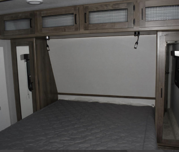 This RV rental bedroom features a comfy bed, modern overhead cabinets with glass inserts, and convenient reading lights.. Keystone RV Sprinter Campfire Edition 2020