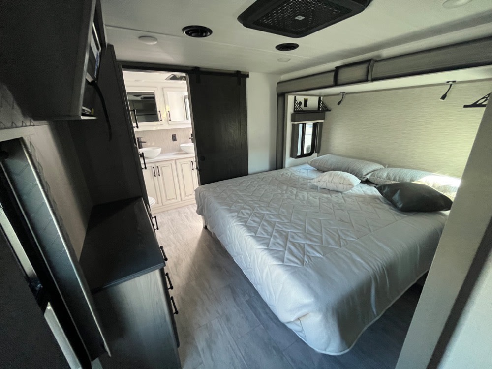 RV rental interior: bright bedroom with a bed and a view into the stylish bathroom. Ideal for comfortable travel.. Keystone RV Montana Legacy Edition 2023