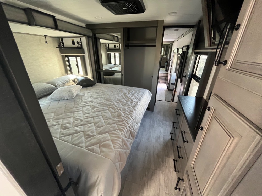 Explore this RV rental's spacious bedroom featuring a large bed, mirrored wardrobe, dresser, and hallway access.. Keystone RV Montana Legacy Edition 2023