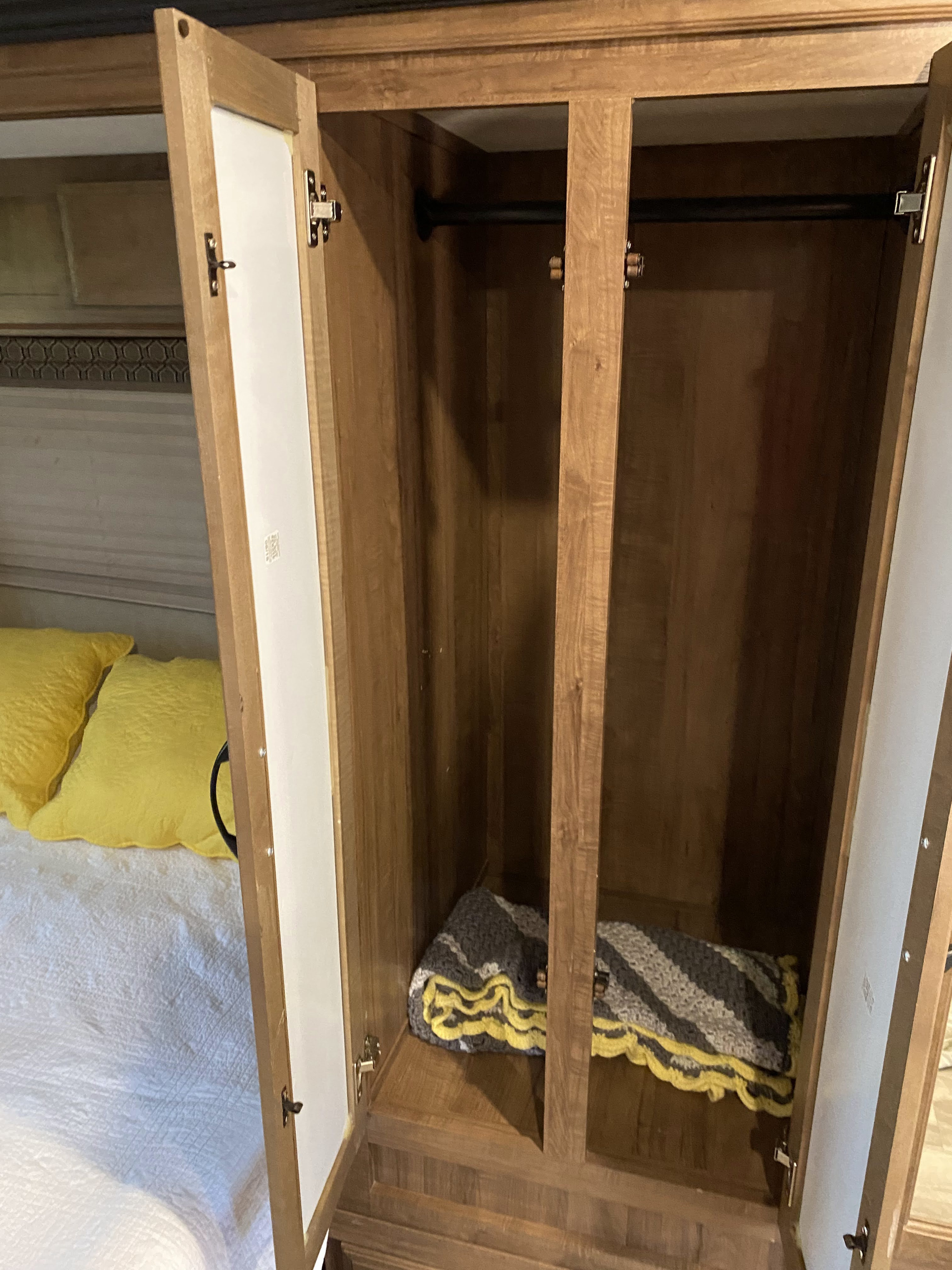 RV rental bedroom closet: open wooden wardrobe with hanging rod & blanket, adjacent to a bed with yellow pillows.. Gulf Stream Conquest 2019